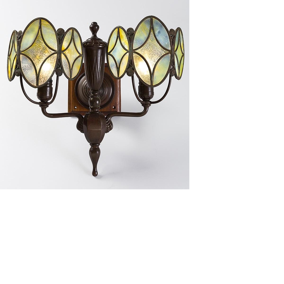 A pair of Tiffany Studios New York patinated bronze and Favrile glass two-armed sconces with opalescent multi-hued shields. Each shield is comprised of three leaded glass oval panels, which are each composed of five pieces of glass. The central