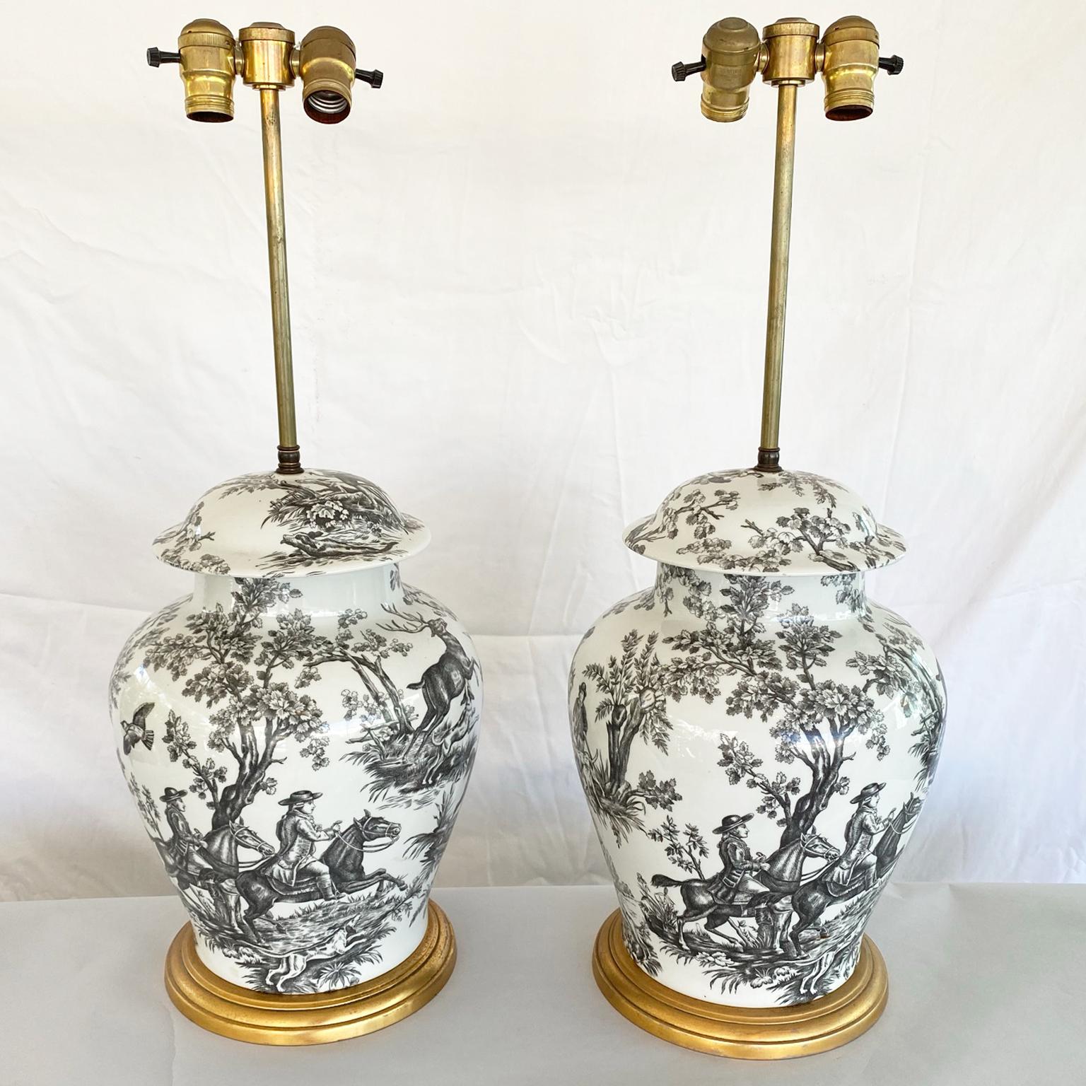Pair of porcelain lidded urns, in ginger jar form, decorated in a black and white toile hunt scene, on graduated giltwood base. 

Stock ID: D9365.