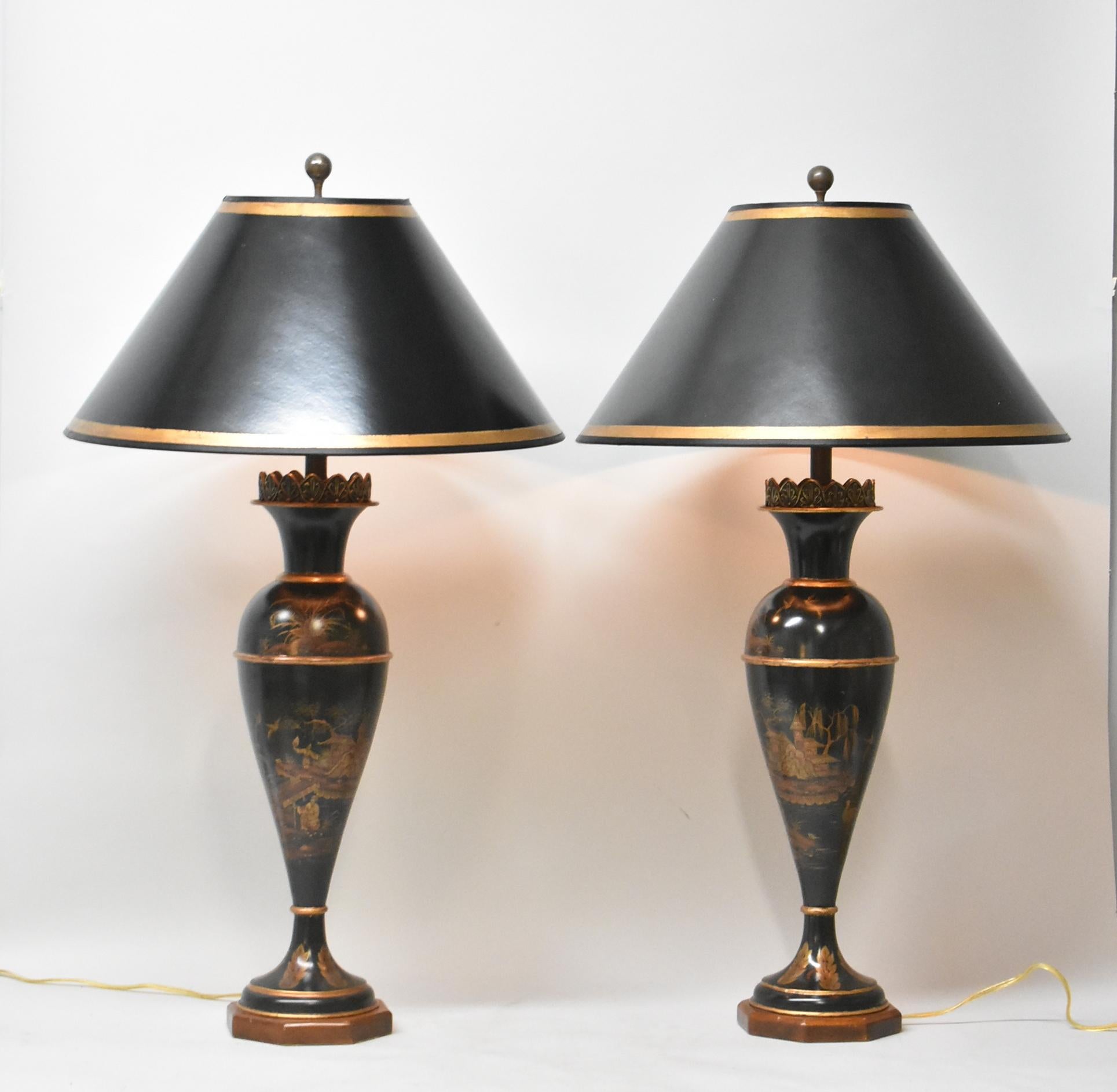 A pair of Asian style table lamps. They feature a black lacquer metal body with Asian scenes in gold tones, a mahogany hexagon base, a three-way switch and a heavy brass finial. The dimensions are 38.5