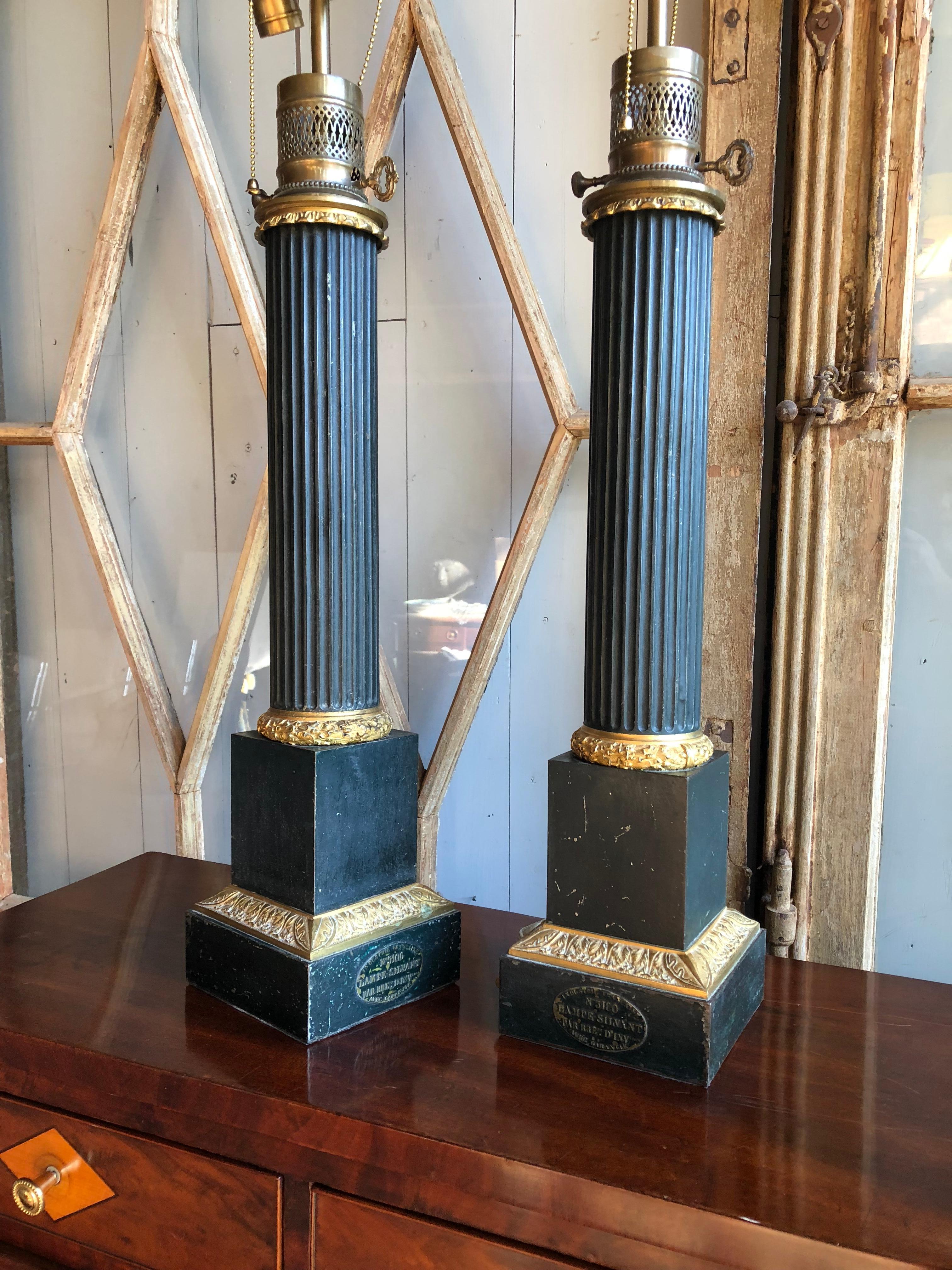A pair of fluted column-form table lamps circa 1800 of impressive size, in dark green painted tole with gilt bronze mounts, converted to electricity from fluid lamps, each marked with a metal label “Lampe-Sylvant”. From the personal collection of
