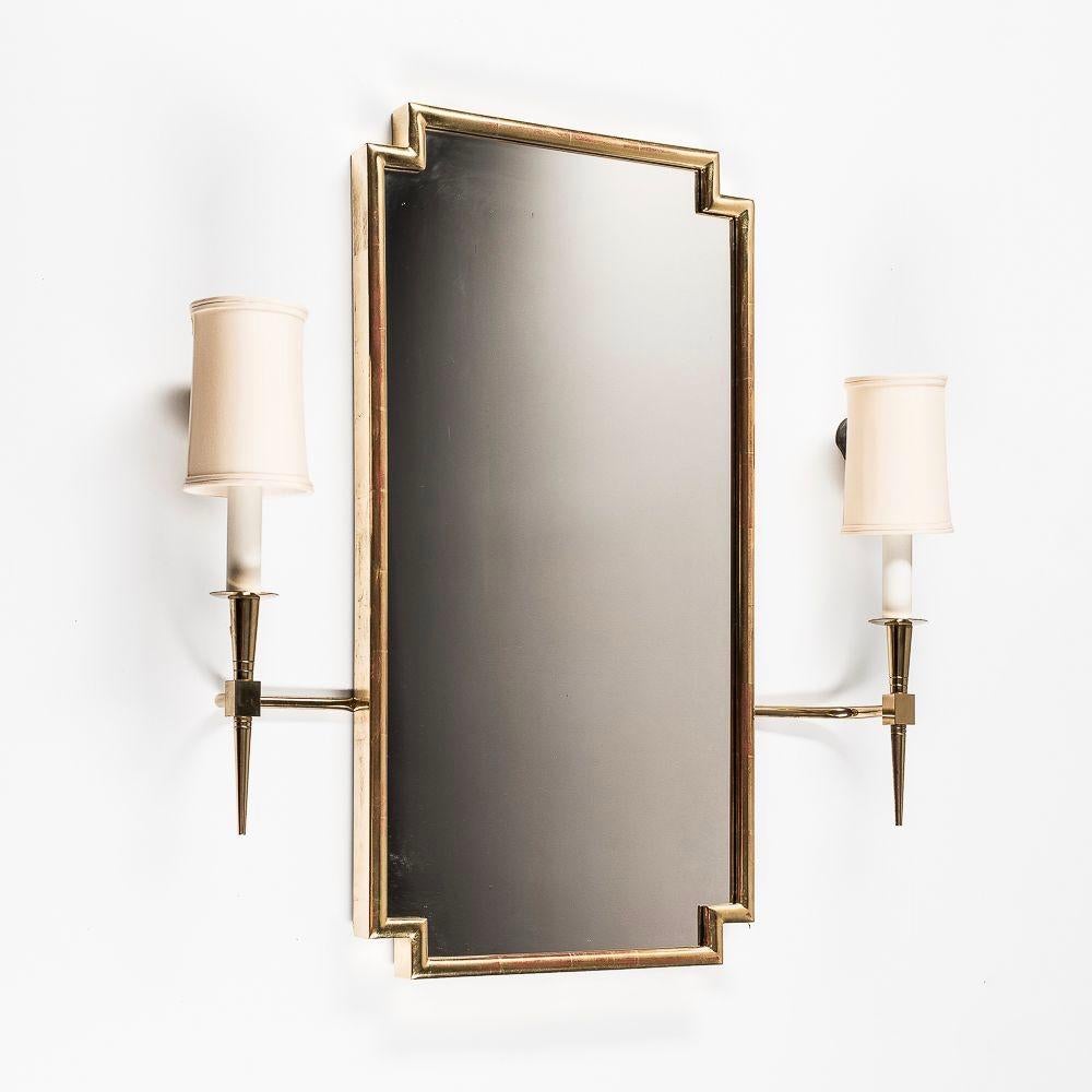 A beautifully made carved and gilt wood rectangular geometric mirror, flanked by a pair of Tommi Parzinger brass sconces, with silk shades. The sconces, which are wired for electricity, attach easily to the wall with brass tabs behind the mirror and