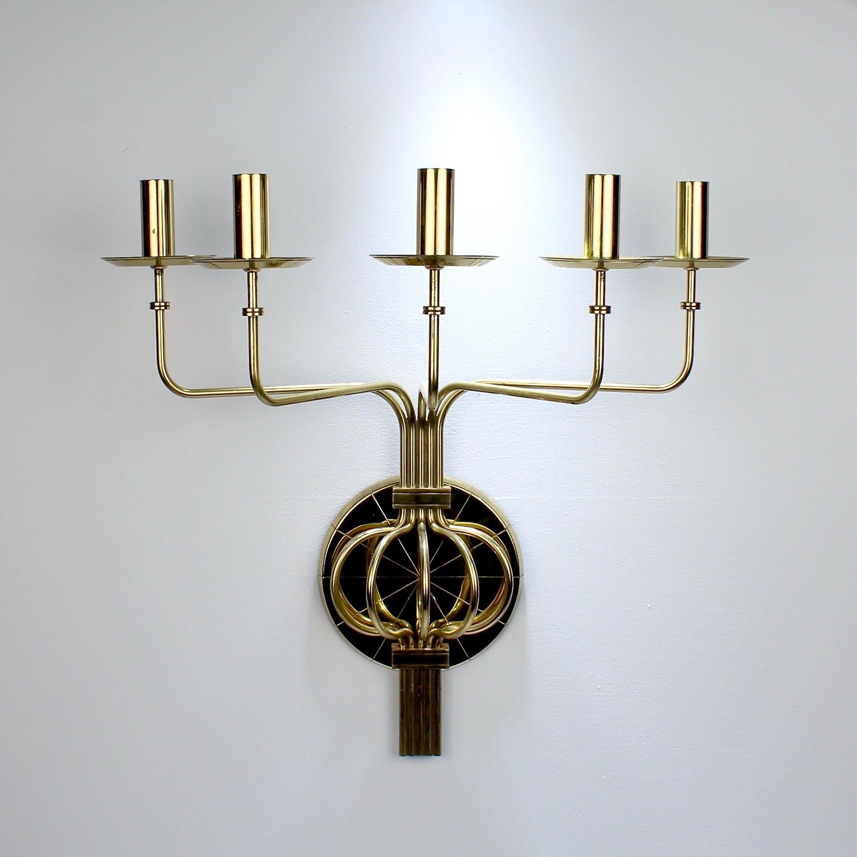 An original pair of iconic Tommi Parzinger Mid-Century Modern brass wall sconces.

Each with 5 lights (or candleholders) on individual arms that are centered on a round disk. 

One of the largest models designed by Parzinger.

Marked for
