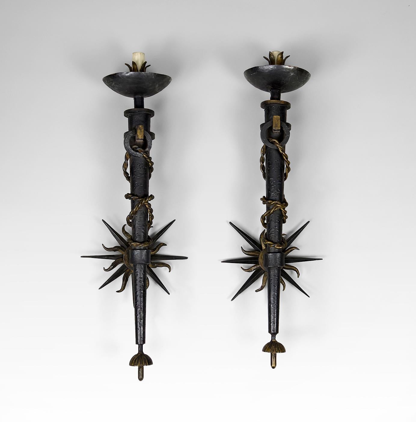 Pair of torch/torchiere sconces.
In patinated and partially gilded wrought iron, the cone-shaped body decorated with a cord, completed by a smei-spherical cup at the top and a gadrooned cup at the base, the sun-shaped wall plate with double patina