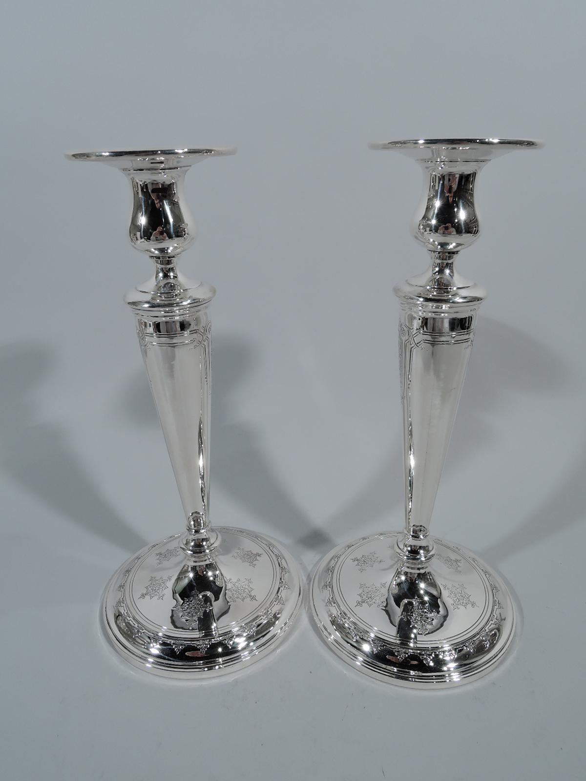 Pair of sterling silver candlesticks in Seville pattern. Made by Towle in Newburyport, Mass. Each: Straight and tapering shaft on raised foot. Bulbous socket with wide and molded rim. Ornament includes pendant garlands in curvilinear frames and