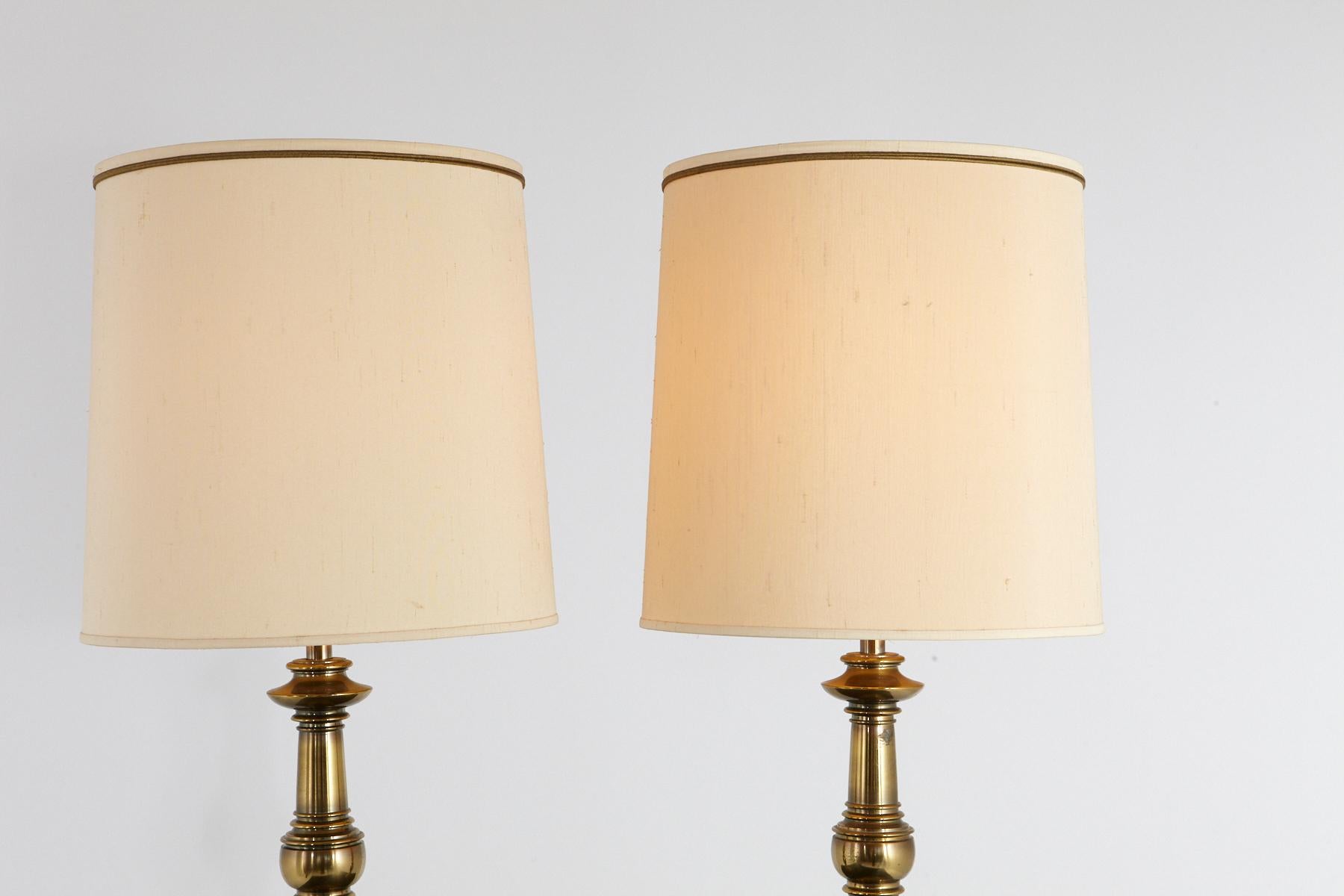 Pair of traditional Stiffel burnished brass table lamps with the original ivory colored drum shades, 
circa 1950-1960s. Very heavy, solid brass quality.
One lamp has some tarnish on the base, both lamps have a natural brass patina, 
which can