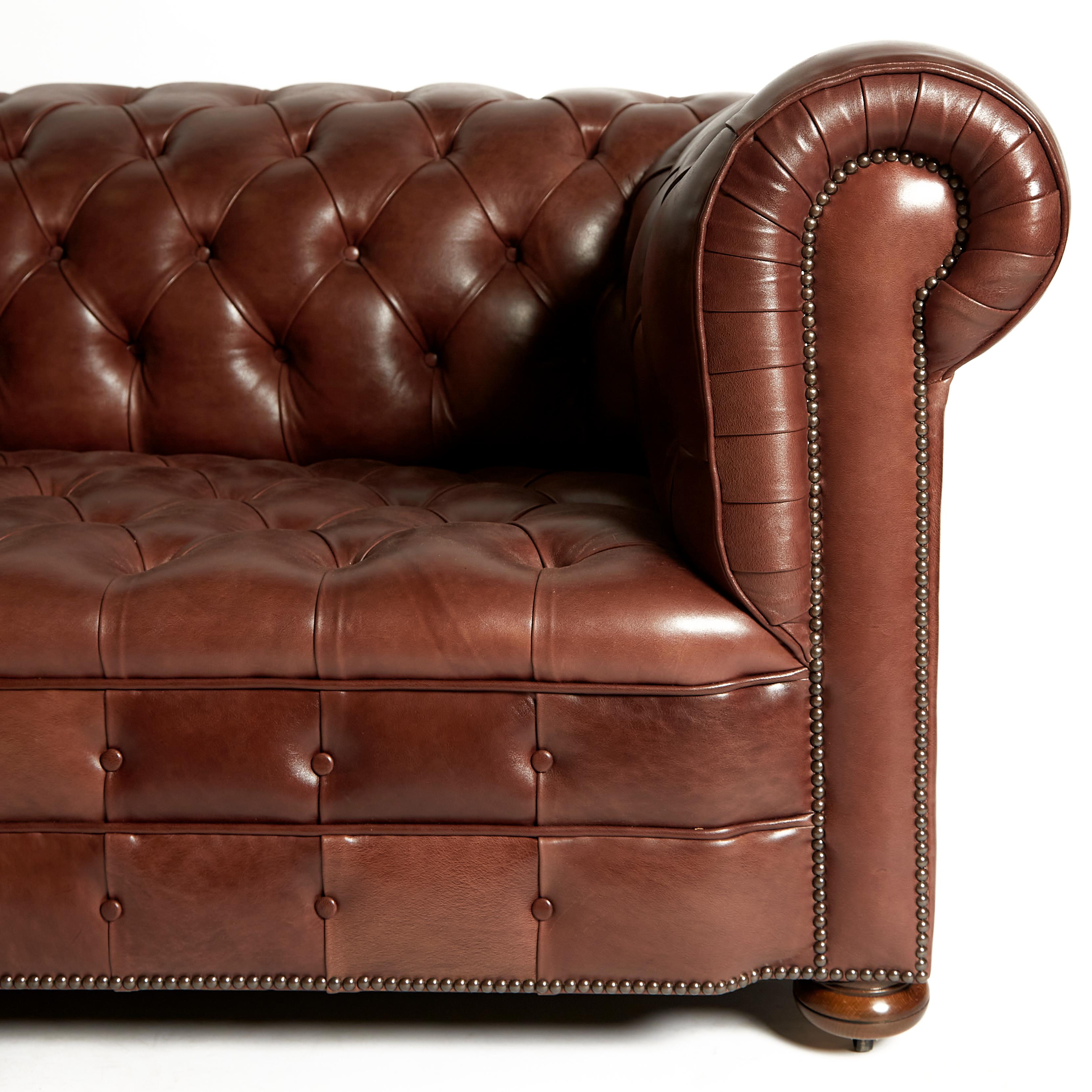 This very handsome and oversized pair of traditionally designed Chesterfield sofas are upholstered in a deep buttoned chocolate brown leather. The sofas feature wide roll back arm rests and stand on mahogany bun feet. Each sofa measures 104 in -