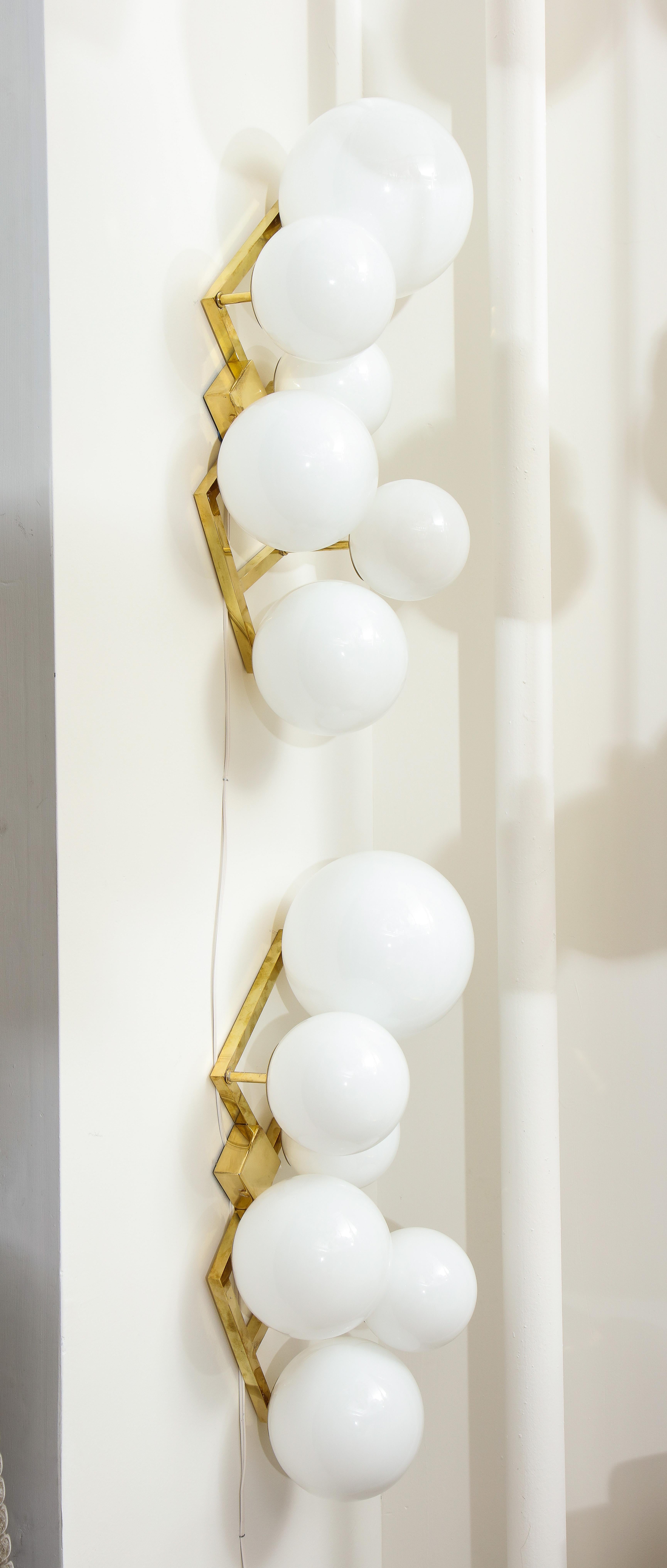 Unique pair of sconces or wall lights consisting of 6 white translucent Murano glass globes or spheres of various sizes attached in an asymmetrical pattern onto a polished brass frame. Wired for U.S. use. For purposes of display in our showroom, we
