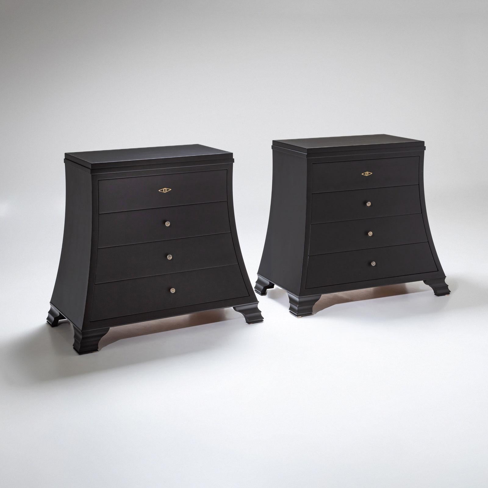 A pair of elegantly designed, black lacquered commodes from the late 20th century. The commodes feature a bold trapezoidal shape and four drawers, offering ample storage space.

Subtle brass fittings add refined accents, emphasizing the clean,