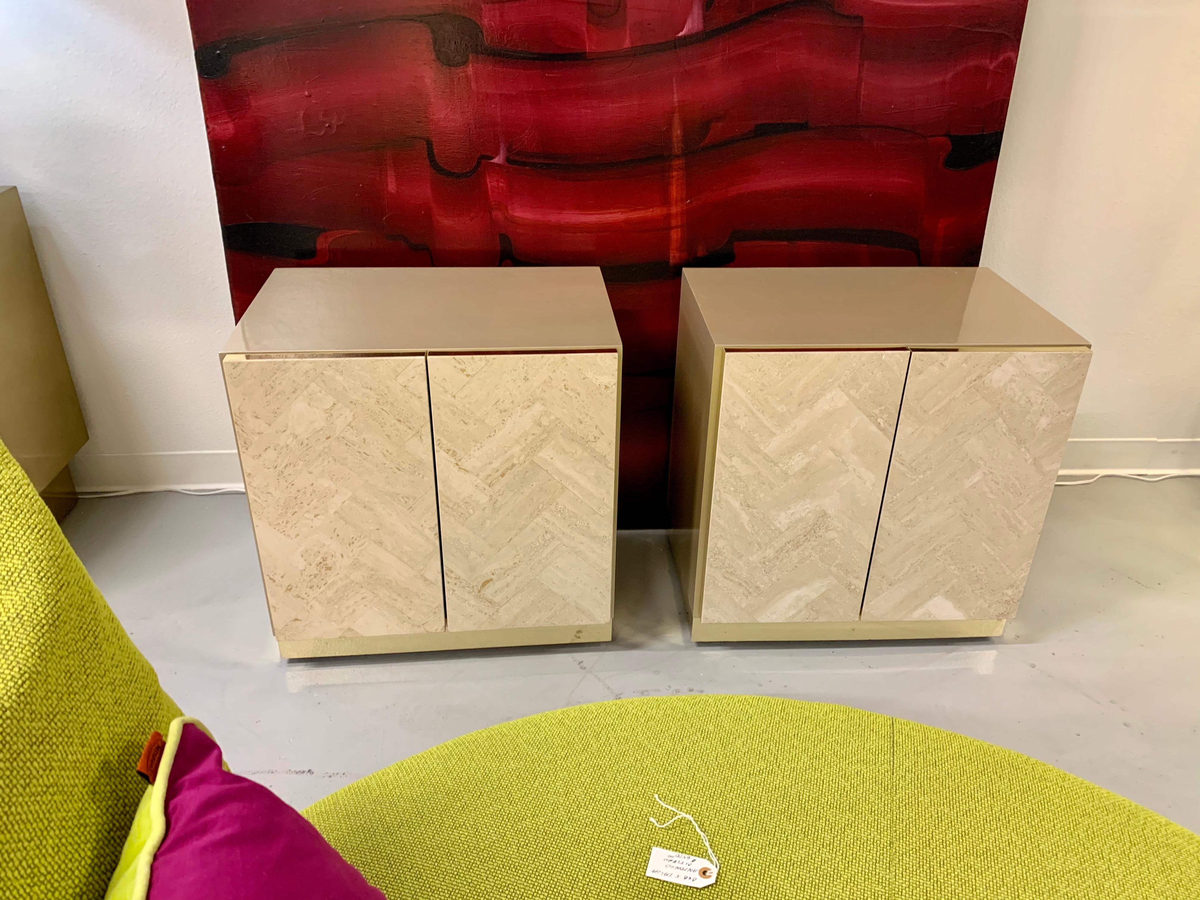 A pair of nightstands with travertine fronts. These were made by Ello and have been just repainted in a beautiful champagne color on the tops and sides. They feature brass banding on the bases and each have a shelf. These measure approximately 24.5