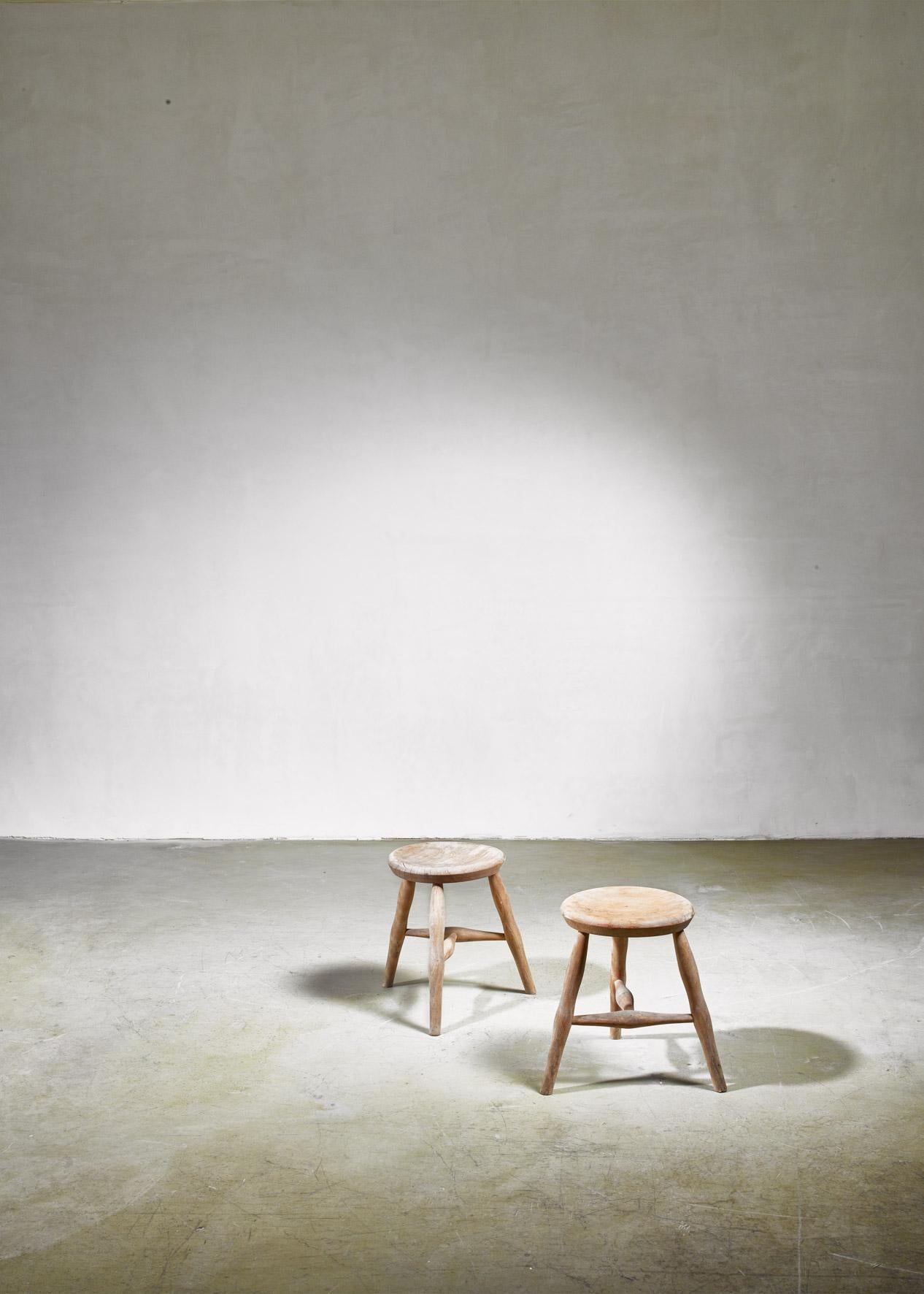 A pair of oak tripod stools with a T-shaped cross-bar.
The stools have a round (35 cm diameter) seating and can also double as side tables.