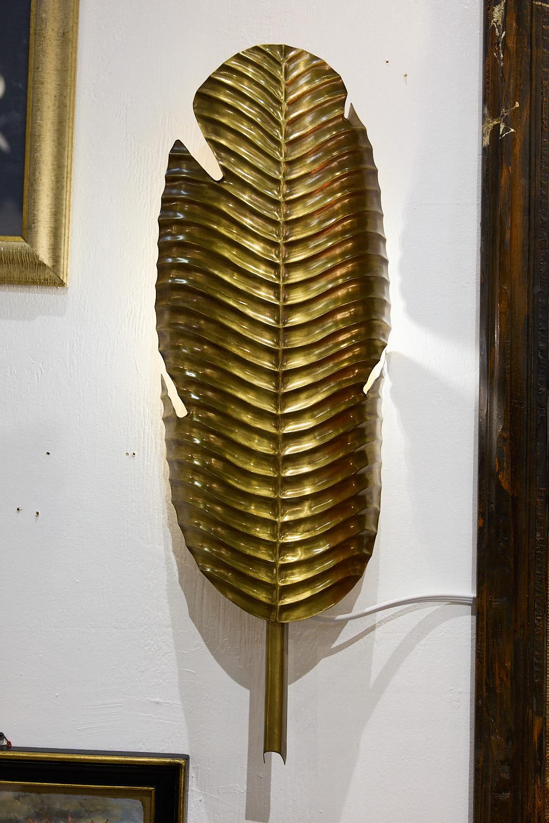 Wonderful pair of large Tropical Leaf Wall Sconces by Currey and Company made of brass and cast in the shape of palm leaves with ridged venation patterns and short stems. A circular wall mount affixes the piece into place, while a single bulb rests