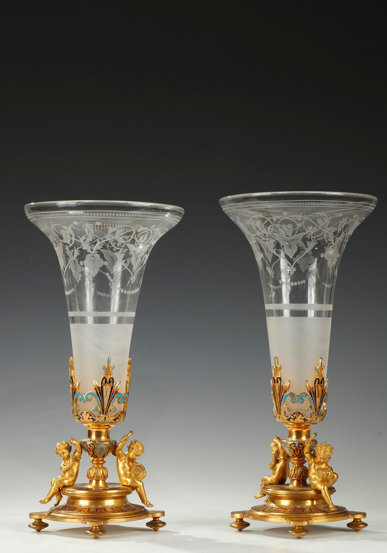 Elegant pair of trumpet-shaped vases attributed to A. Giroux, with flare neck in engraved crystal decorated with leafy interlacing and beads friezes. Removable, they are enclosed in circular pedestals in gilded bronze adorned with enameled geometric
