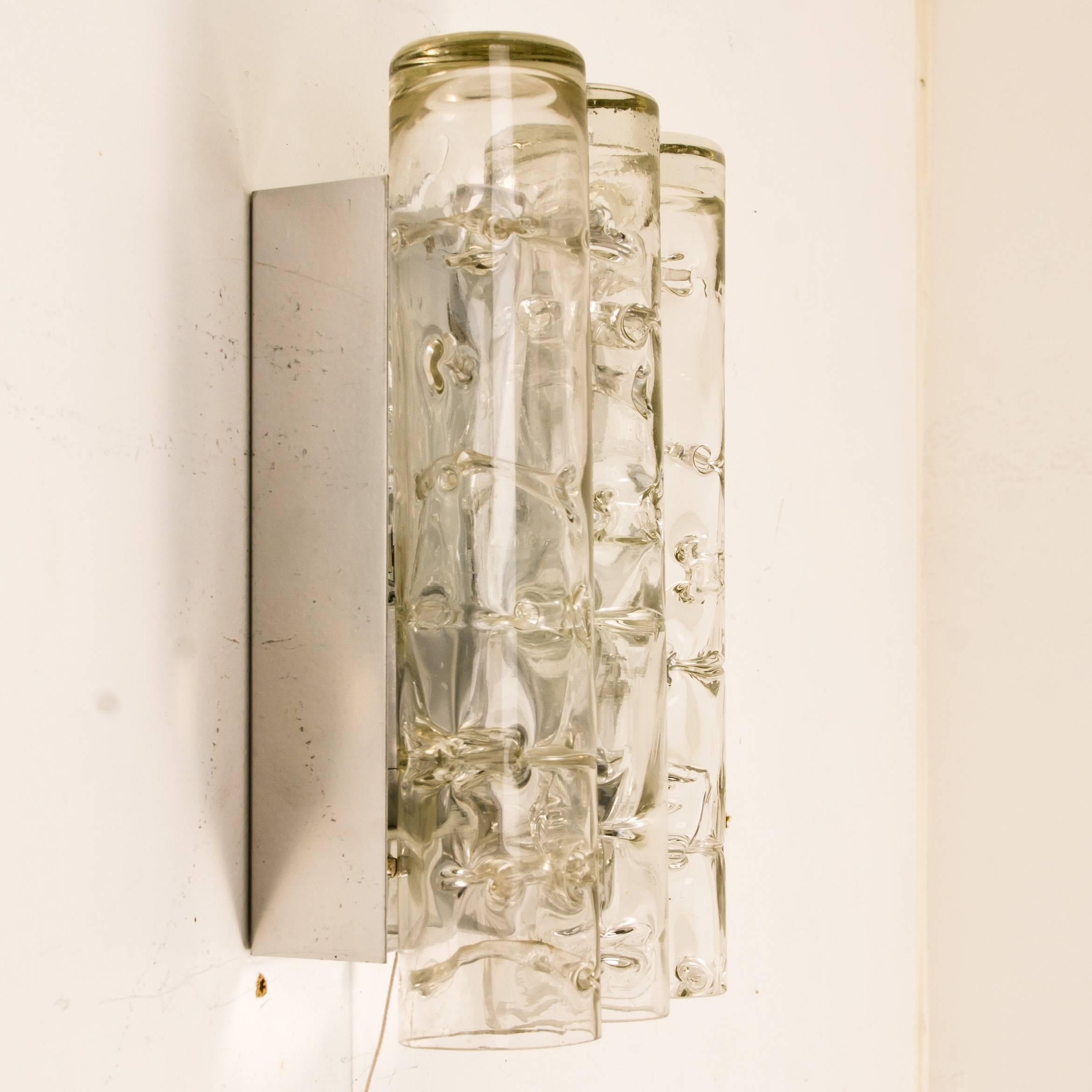 Diese Wandlampen sind von Doria entworfen. Die Wandleuchte ist aus Aluminium gefertigt und verfügt über drei dicke mundgeblasene Glasröhren. Die Lampe nimmt E14 max. 40W Glühbirnen. Die hochwertigen großen quadratischen Kristallwürfel reflektieren