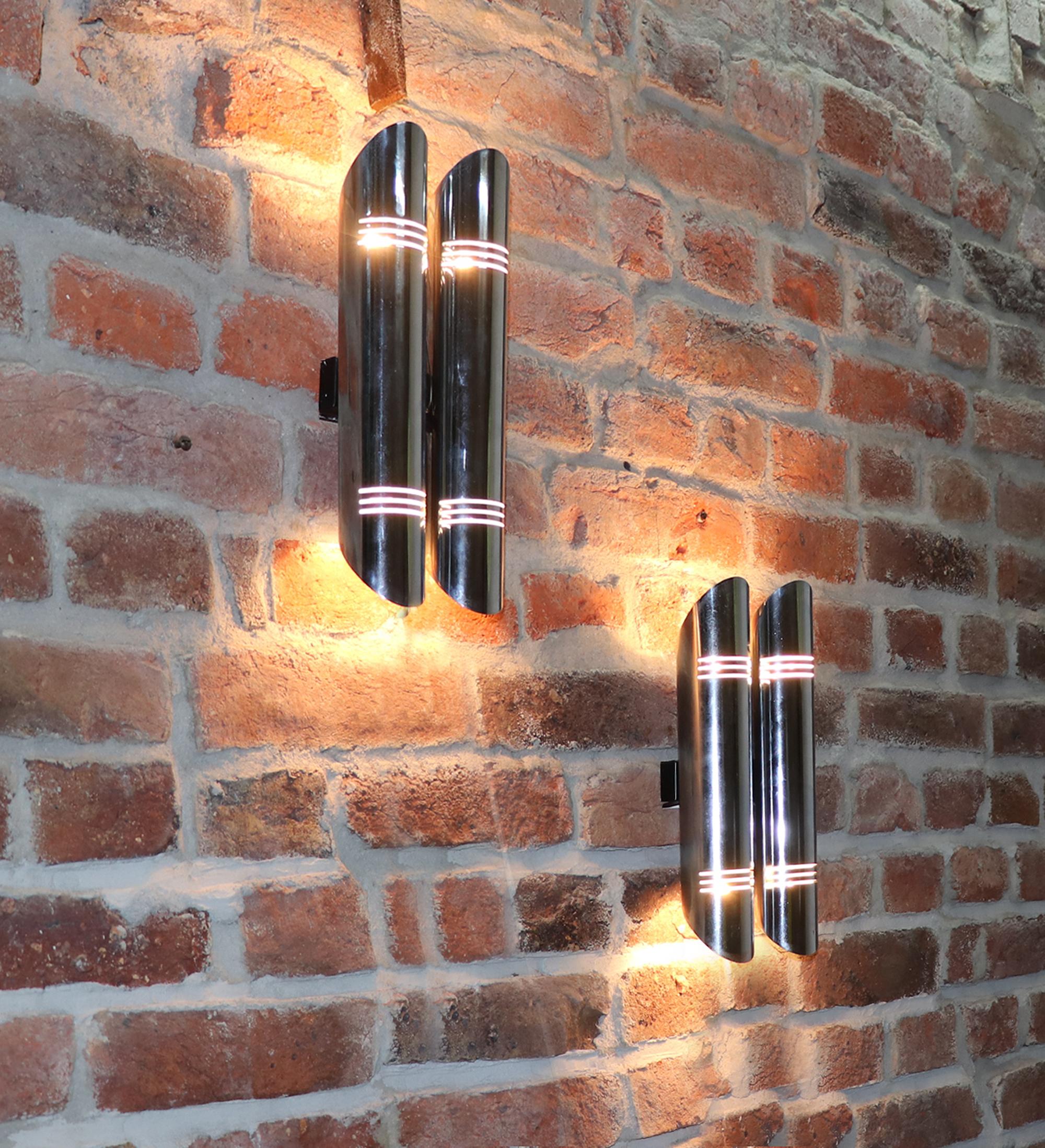 Elegant pair of tubular wall sconces in chromed metal made in the 1970s. 

Style: Space Age. 
Measures: height 12.4“ in. (31,5 cm), width 5.3“ in. (13,5 cm), depth 3.3“ in. (8,5 cm). 
Lighting: takes two small Edison E14 base screw bulbs per sconce.