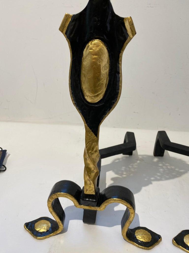 This stylish set of English andirons were acquired from a Palm Beach estate and they are fabricated in wrought iron and cast brass. And the pieces are highlighted with gold painted accents.