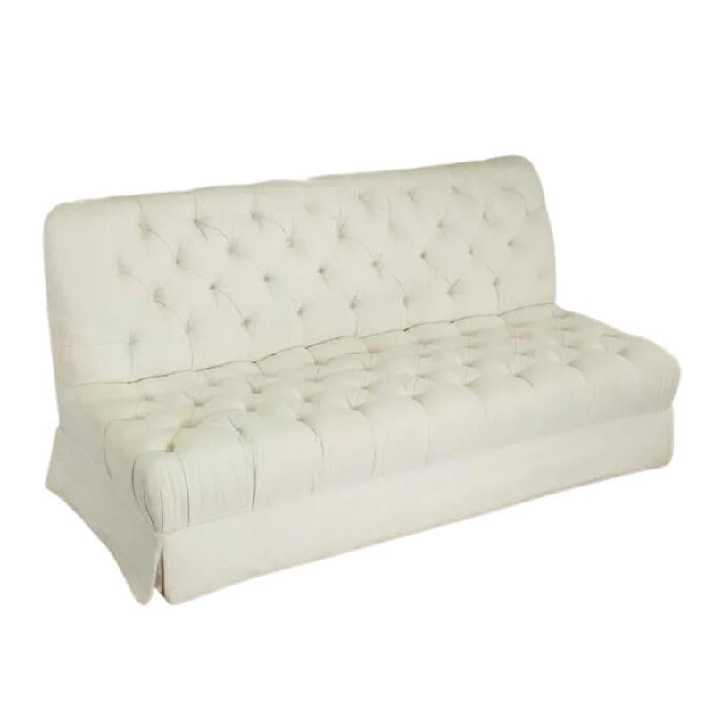 A pair of armless tufted cotton, three seat sofas, from a Daniel Romualdez designed home. The pair of vintage sofas are American made, of textured white cotton with button tufts to seat and back with tailored skirt on all sides.