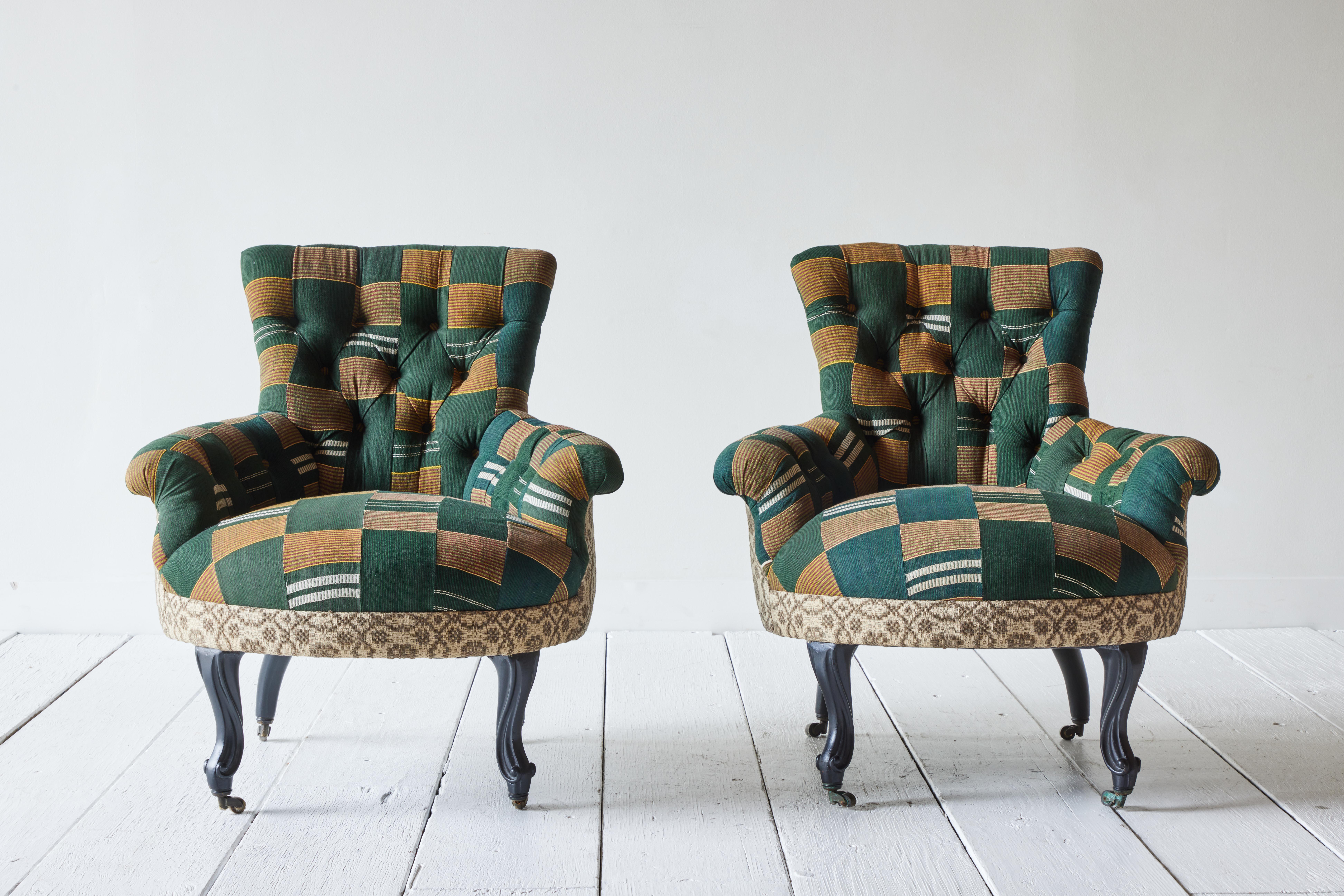 A pair of 19th century French tufted armchairs reimagined with vintage Ewe Kente cloth and Early American textiles. Padded seat raised on cabriole wood legs with brass castor wheels. 
  