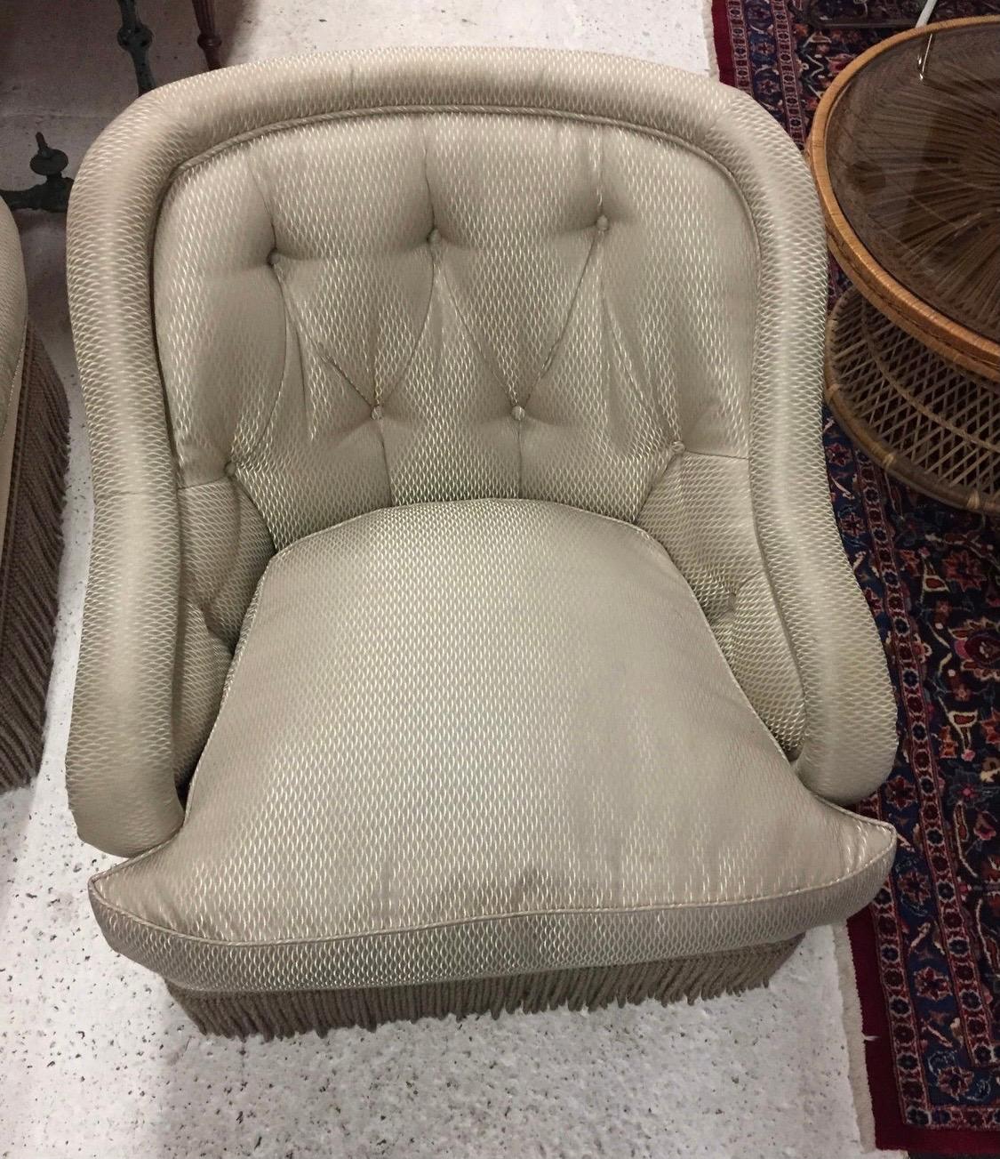 Lovely pair of silver and taupe club chairs with tufted seat backs and down wrapped cushions. The chairs are accented with a fabulous rope fringe trim. They sit very comfortably and have age appropriate wear.