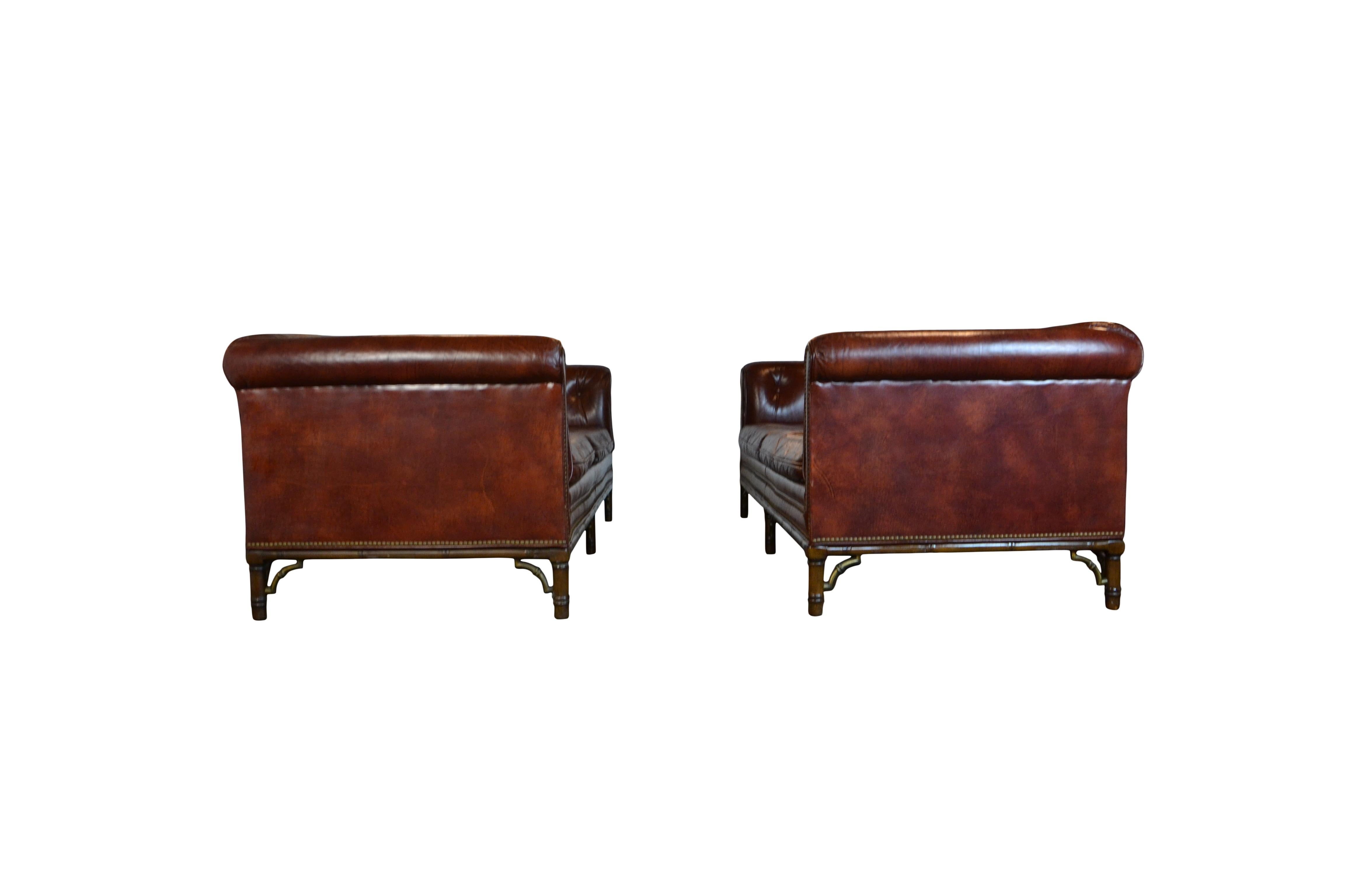 An impressive pair of tufted leather Chesterfield sofa's in a slightly reddish brown upholstery. Wooden faux bamboo frames with brass bracket leg supports.
