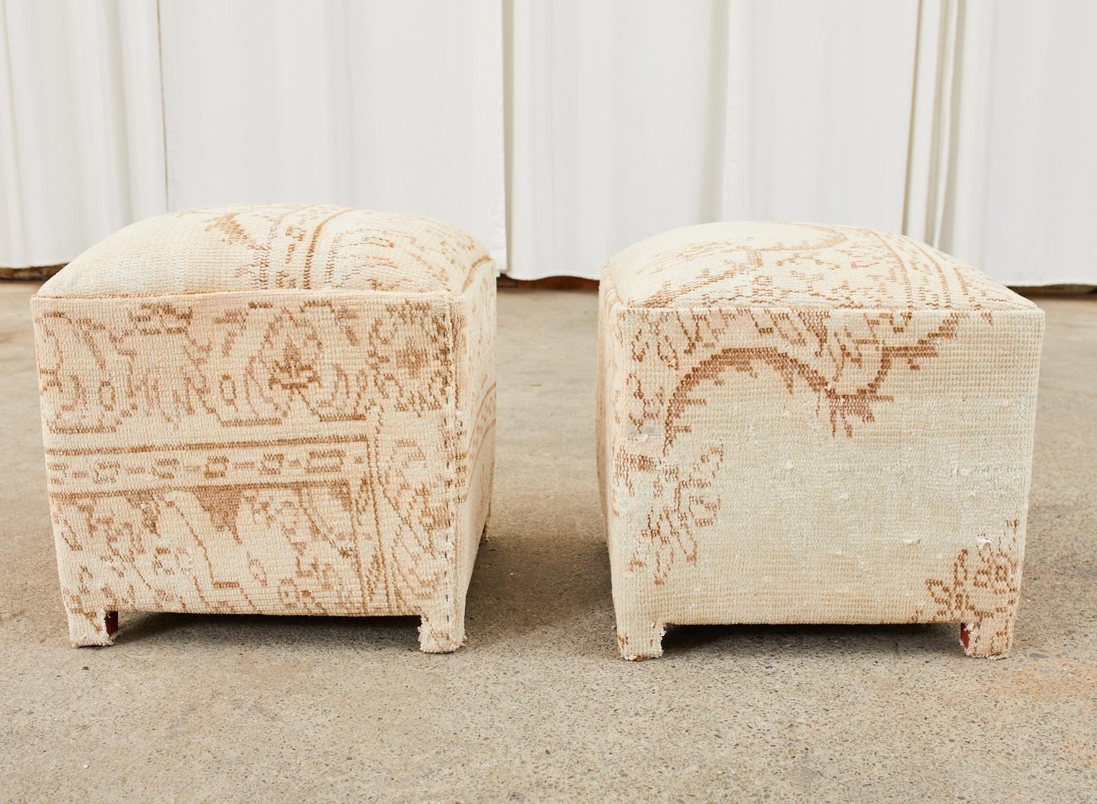 Rustic pair of footstools, ottomans, or poufs featuring a Turkish Kilim style rug upholstery. The square cube forms have a padded, domed top and showcase the aged and distressed patina of the rugs. Supported on each corner with short square feet.