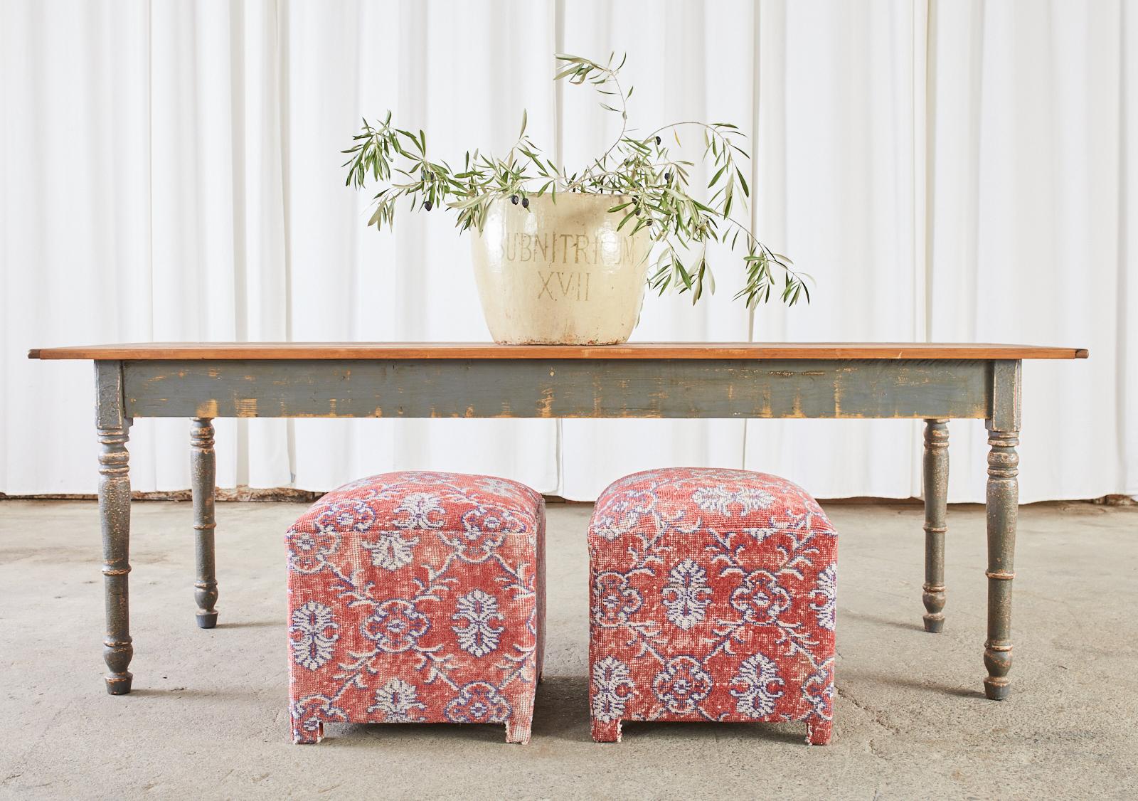 Colorful pair of footstools, ottomans, or poufs featuring a Turkish Kilim style rug upholstery. The square cube forms have a padded, domed top and showcase the aged and distressed patina of the rugs. Supported on each corner with short square feet.