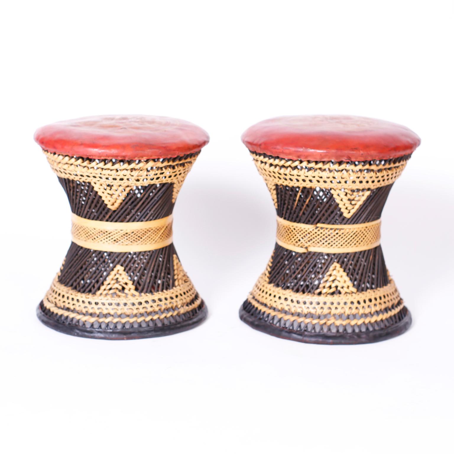 Pair of ottomans with soft oxblood leather tops embossed with classical scenes over hourglass form wicker bases.
