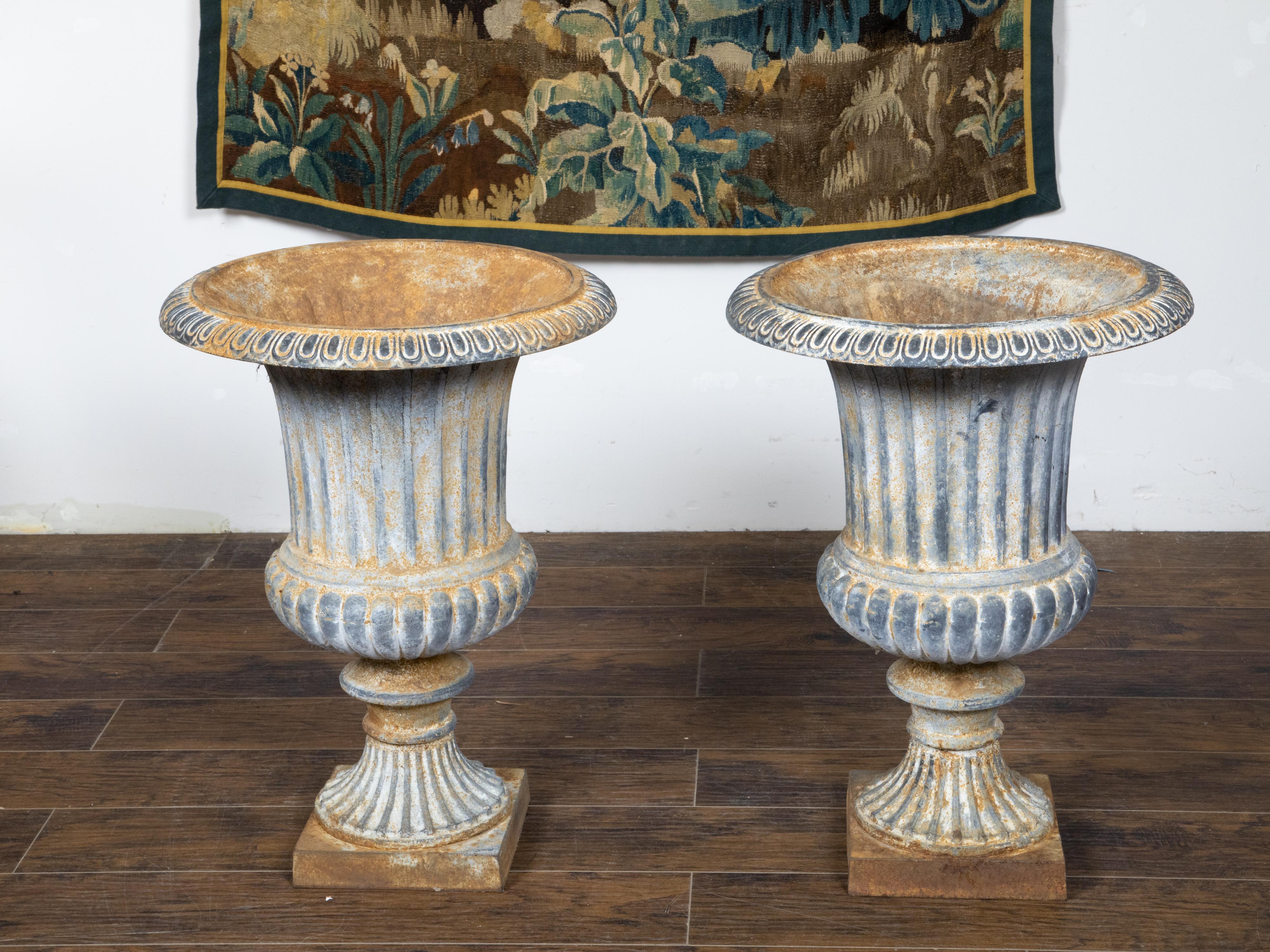 A pair of French turn of the century cast iron Medici urn planters from the early 20th century, with flaring lips, gadroon motifs, fluted bodies and square bases. Created in France at the Turn of the Century which saw the transition between the 19th