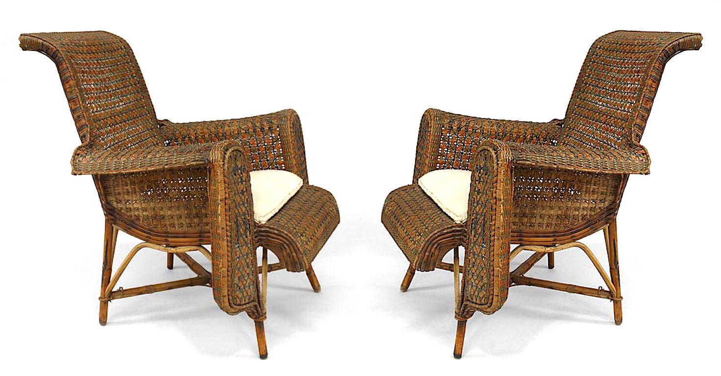 Pair of turn of the century French arm chairs composed of natural wicker trimmed in green and orange with woven front arm panels, an upholstered seat cushion, and curved back over four legs joined by an intersecting stretcher.