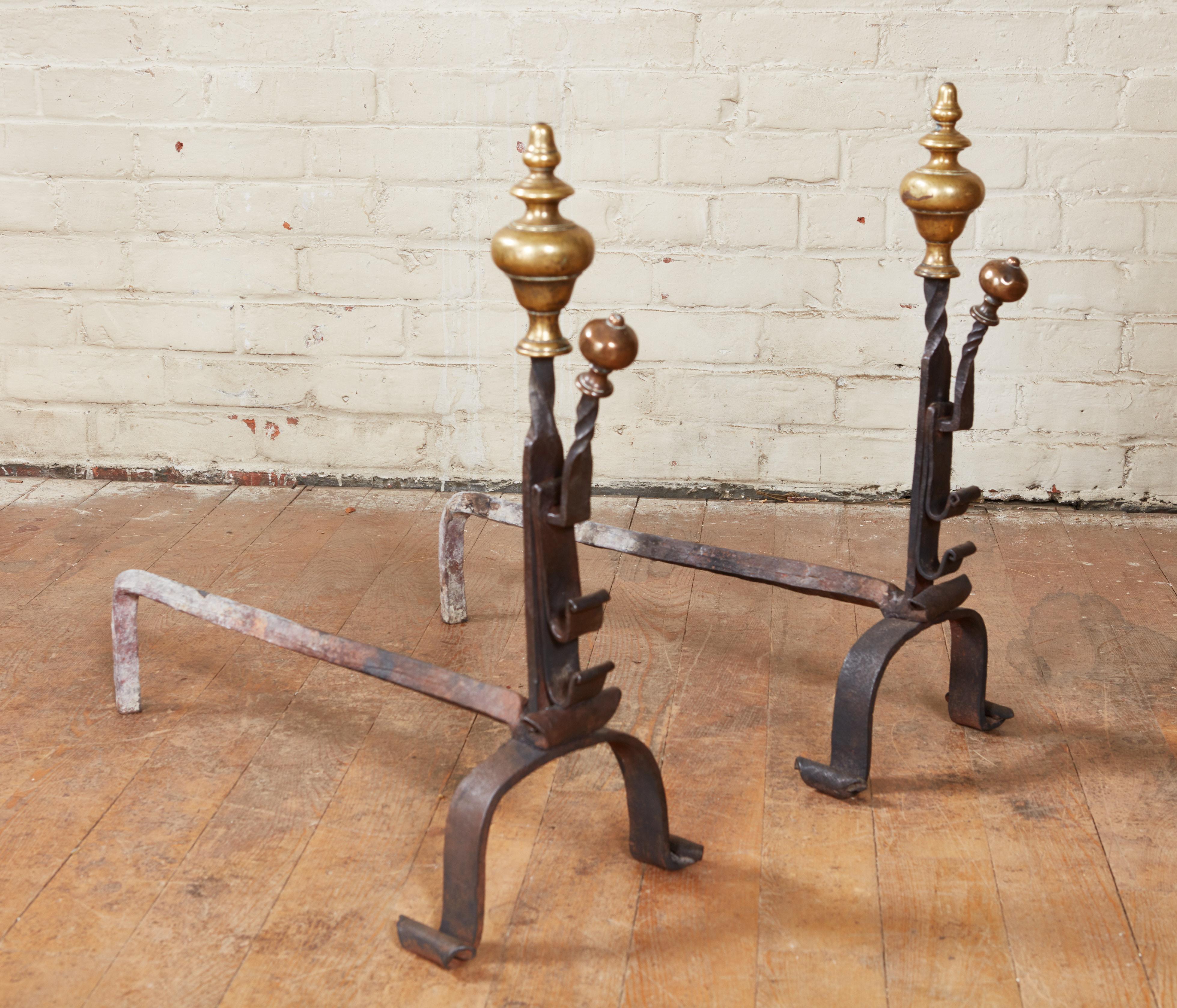 Fine pair of bronze and wrought iron andirons having turned steeple finials over partly twist worked shafts with forward facing bronze onion finials and standing on arched legs ending in scrolled feet.
    