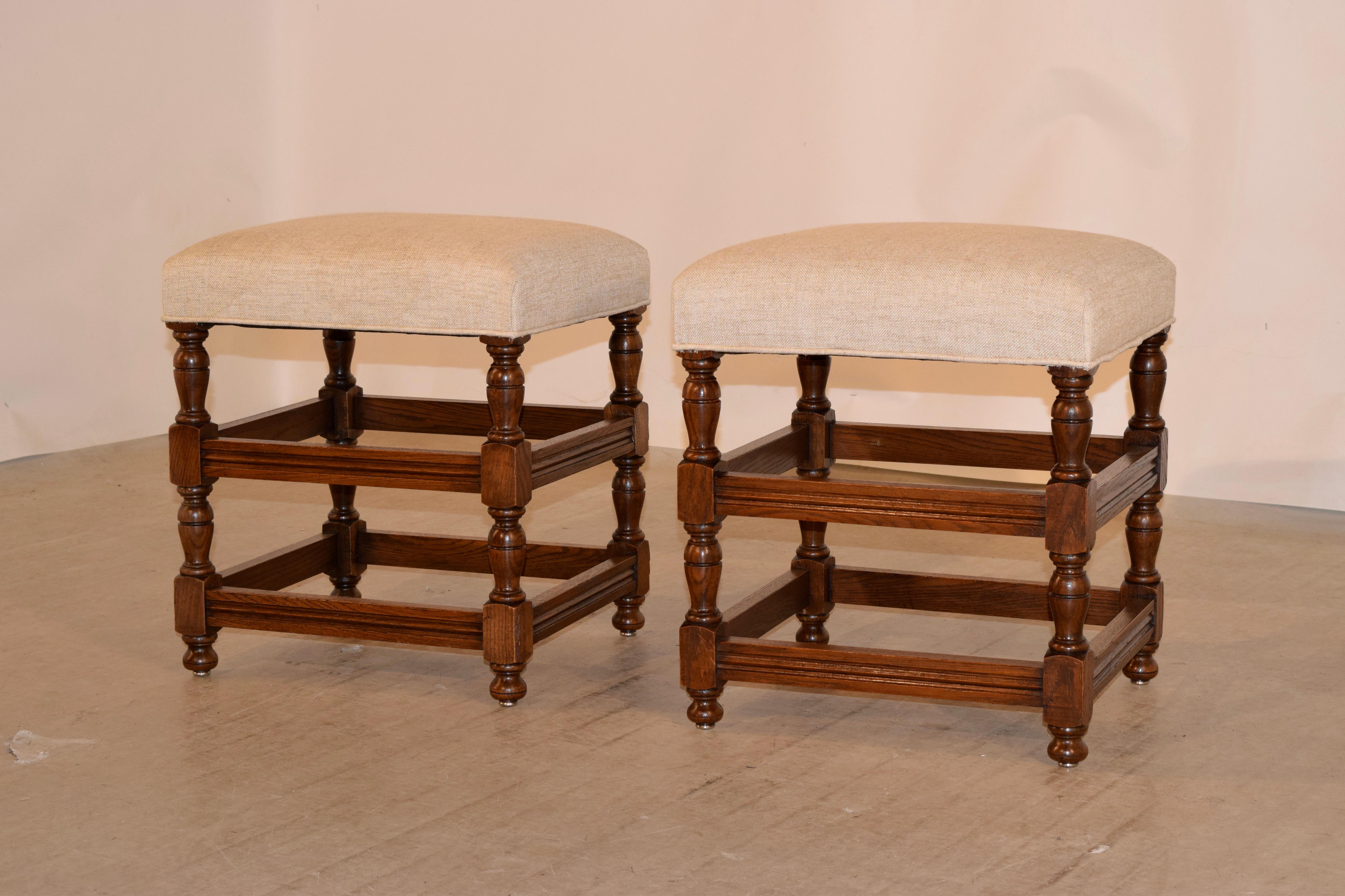 Pair of English oak turned stools with newly upholstered seats in linen. The frames have hand-turned legs joined by molded cross stretchers and raised on hand-turned feet.