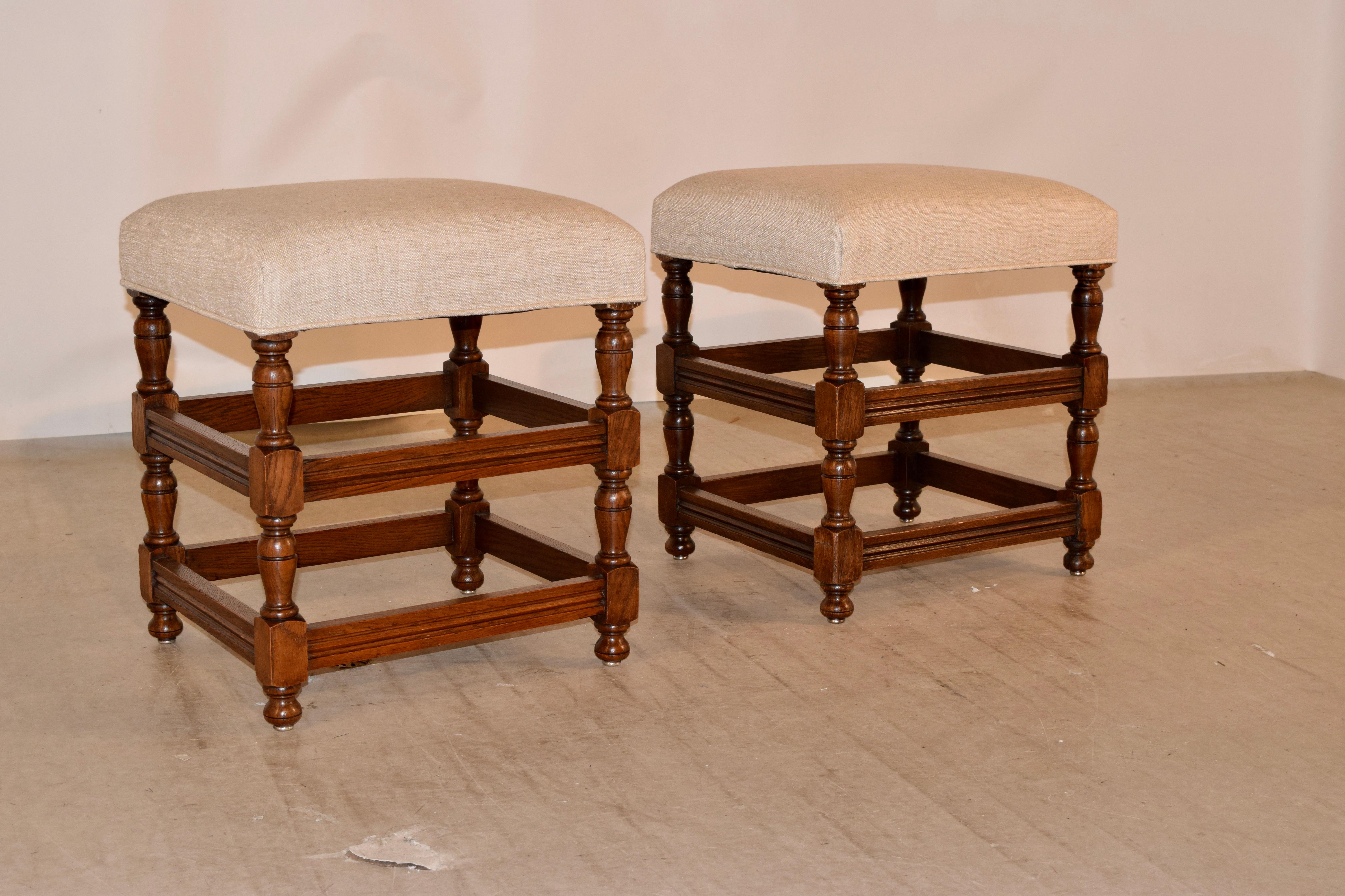 Pair of English oak turned stools with newly upholstered seats in linen. The frames have hand-turned legs joined by molded cross stretchers and raised on hand-turned feet.
 