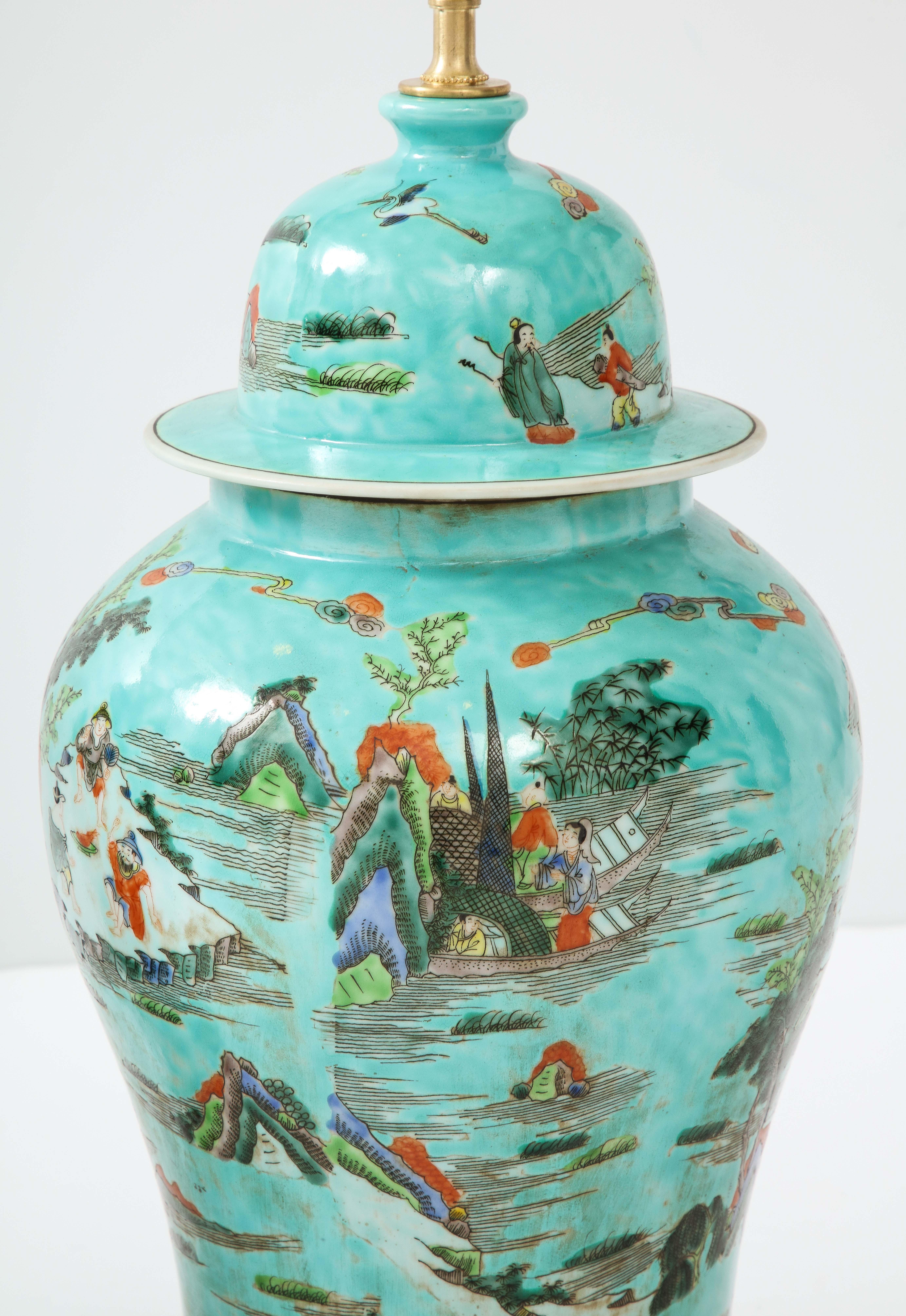 A pair of colorful and fanciful porcelain urns converted to lamps on a giltwood base. The ground color is a beautiful turquoise decorated with a colorful Chinoiserie inspired scene--a great way to add vibrant color to a room.