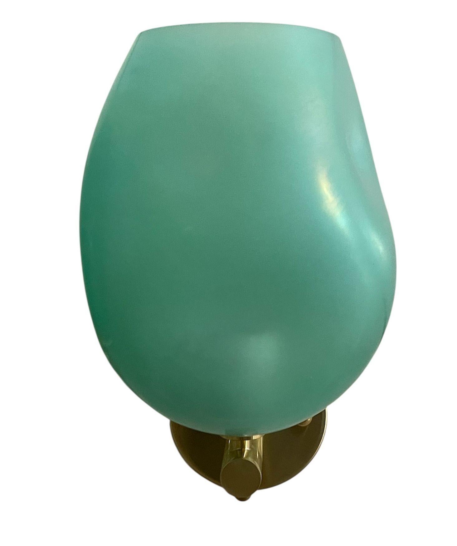Elegante coppia di applique italiane con paralumi in vetro di Murano turchese soffiato a mano con la tecnica del soffio. Le forme organiche e arrotondate del vetro diffondono la luce con un bagliore morbido e luminoso, mentre le cornici in ottone