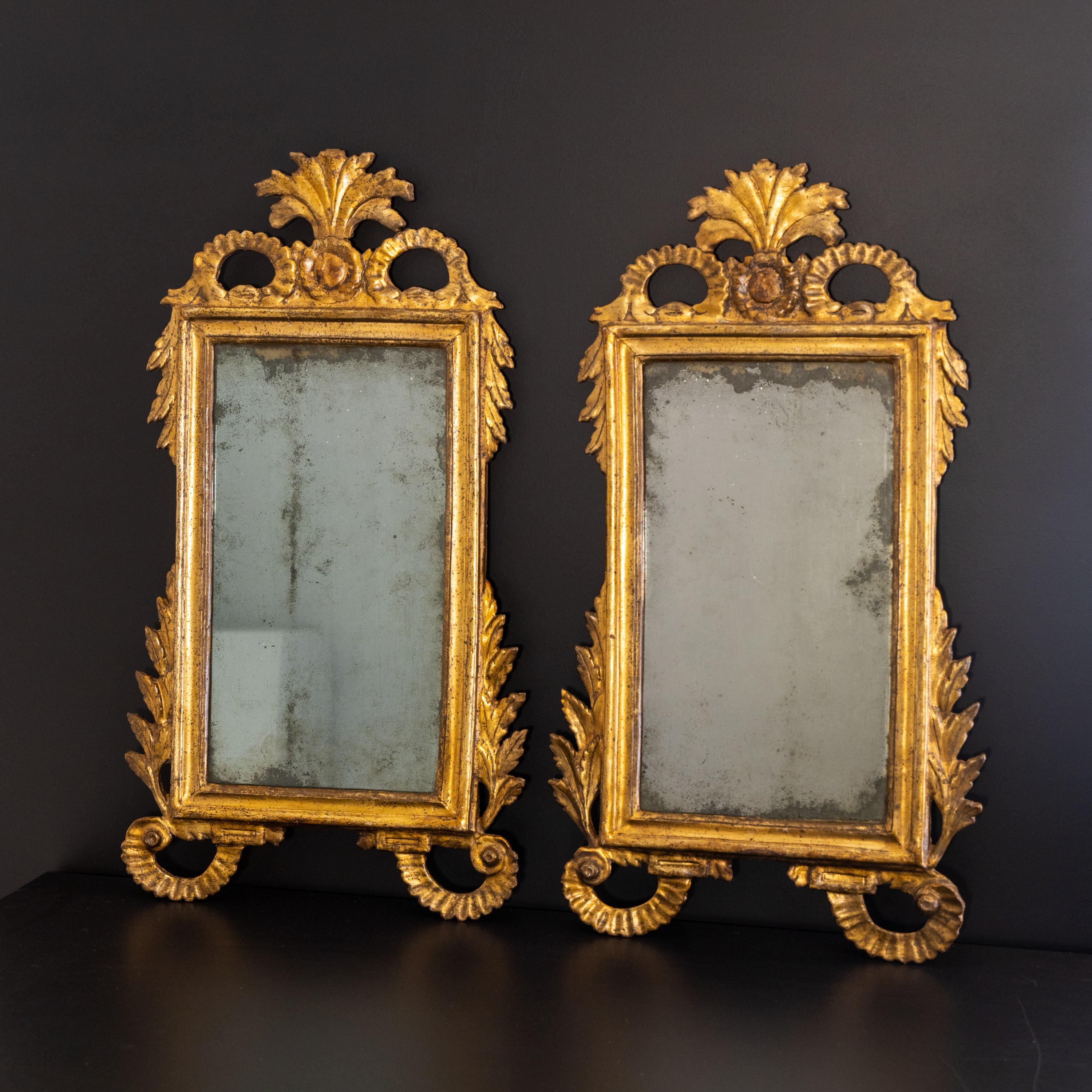 Pair of Italian wall mirrors in gold patinated and stuccoed wooden frames with old mirror glasses.