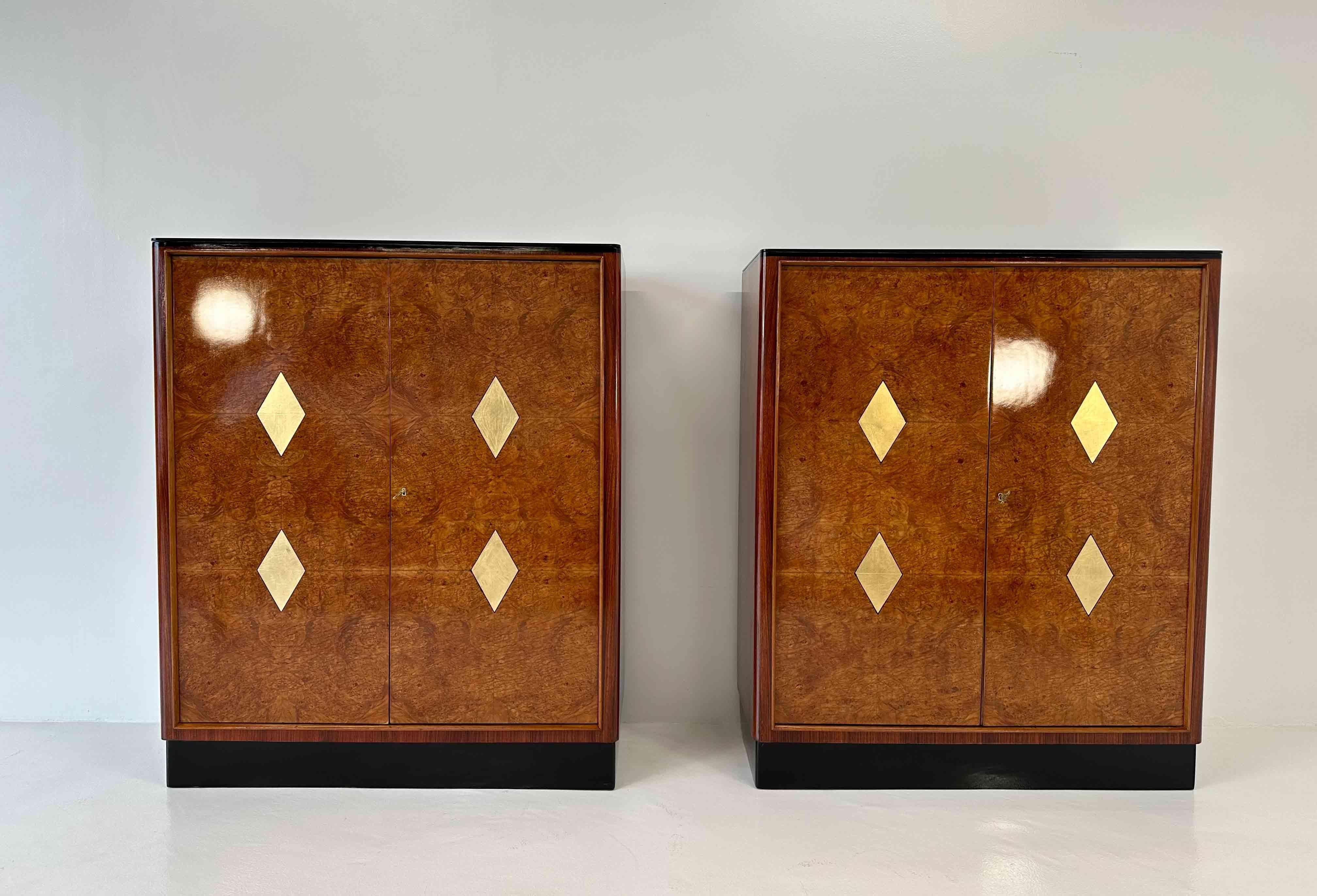 This pair of twin Art Deco cabinet was produced in Italy in the 1940s. 
The two cabinets are in maple briar, with maple profiles and gold leaf decorations in the front. The base is in black lacquered wood, while the top is a black glass. 
Completely