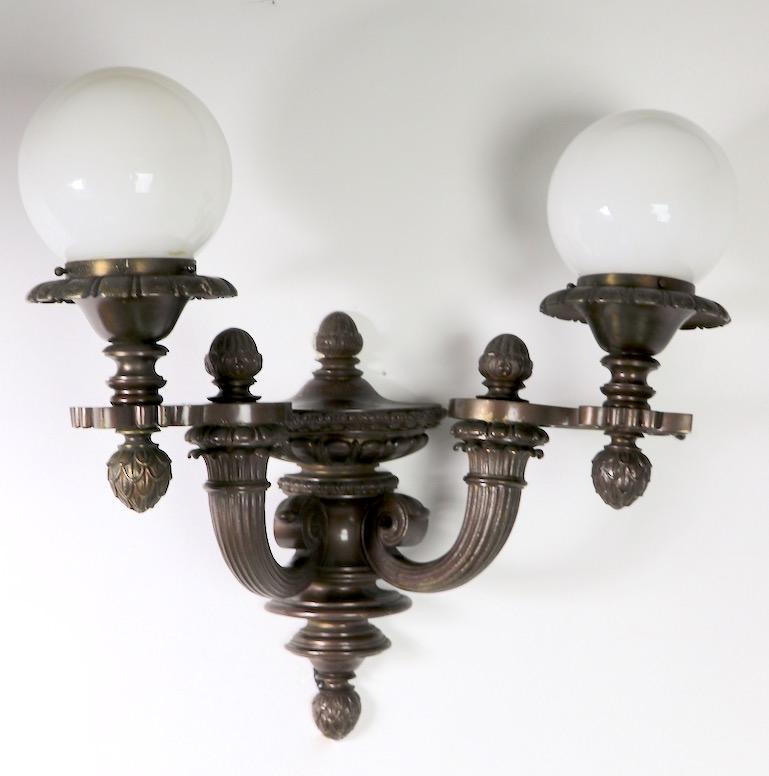 Impressive pair of cast bronze (or brass) architectural scale interior or exterior sconces, in the Beaux Art style. Both are in very good, original and working condition, both include glass ball globes (5 inch dia. x 3.5 inc neck ) and original