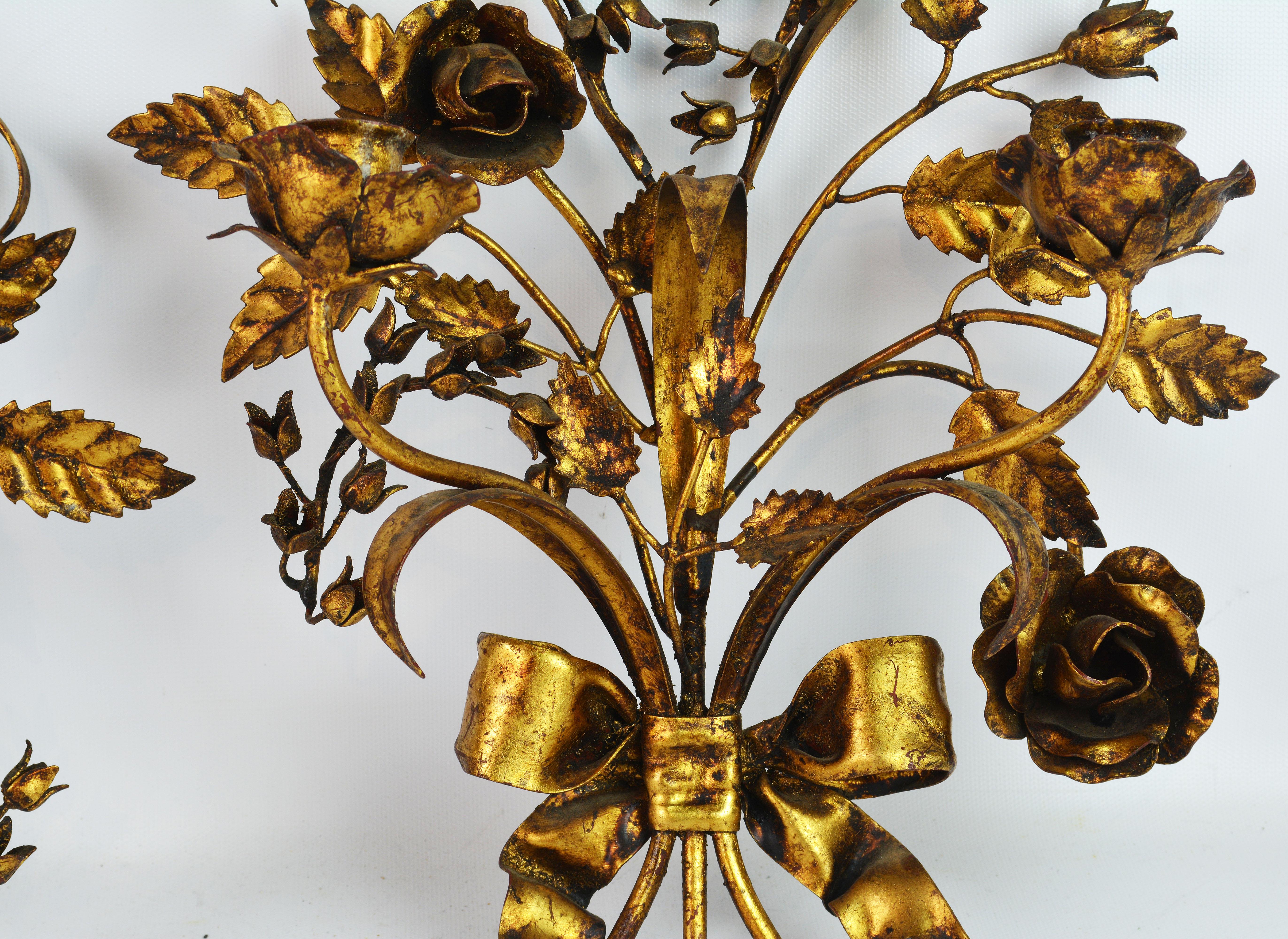 This is a very decorative pair of Italian mid-20th century gilt tole sconces designed like a bouquet of flowers and leaves held together by ribbons and featuring two candle holders each.