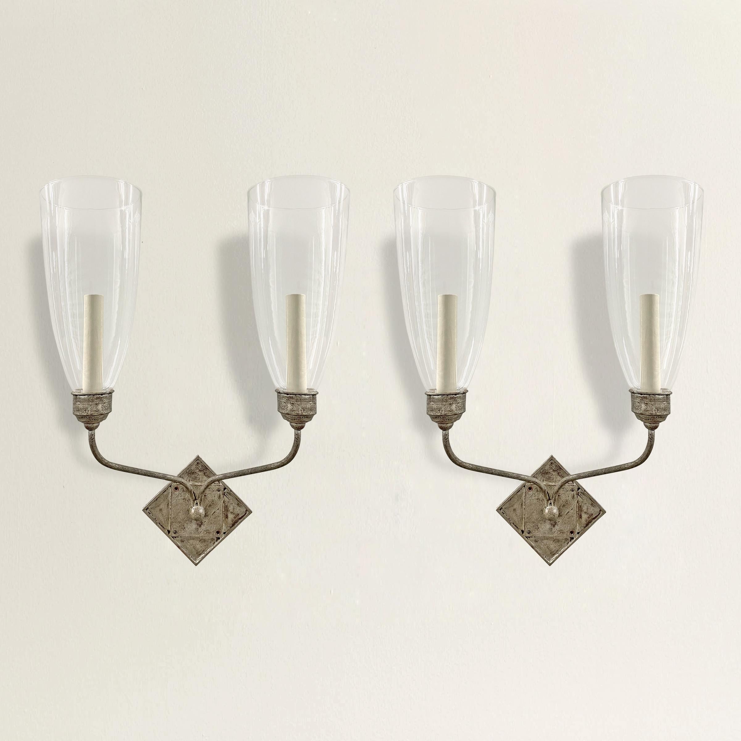 A pair of two-arm sconces with diamond backplates, a silver-leaf finish, and each with two tall blown glass hurricanes. Wired for US; candelabra bulbs.