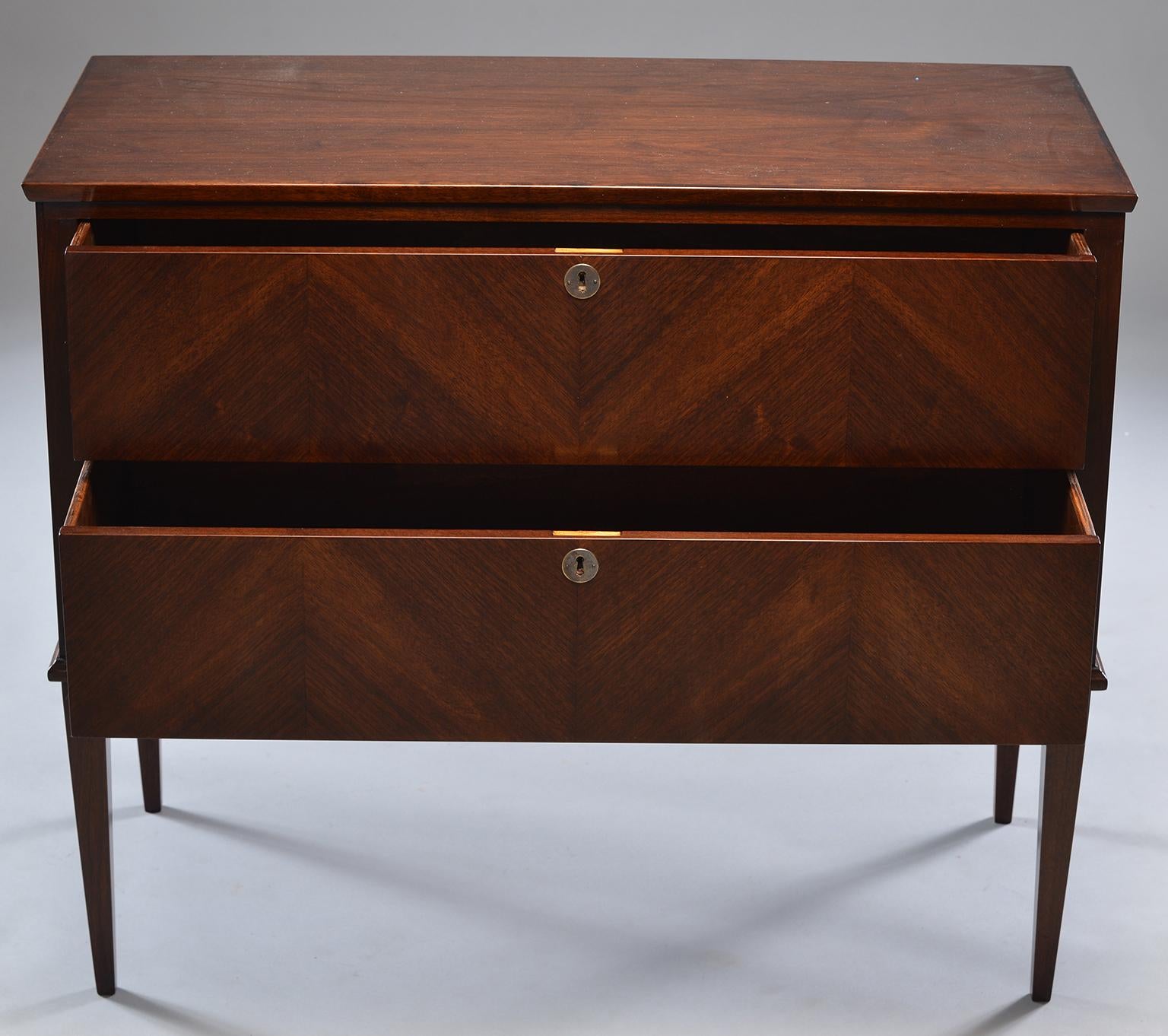 This pair of walnut Empire style chests was custom-made by an English cabinet maker. Each chest has two functional locking drawers. Drawer fronts have decorative pattern formed by placement of veneer so that graining / wood figuring forms chevron