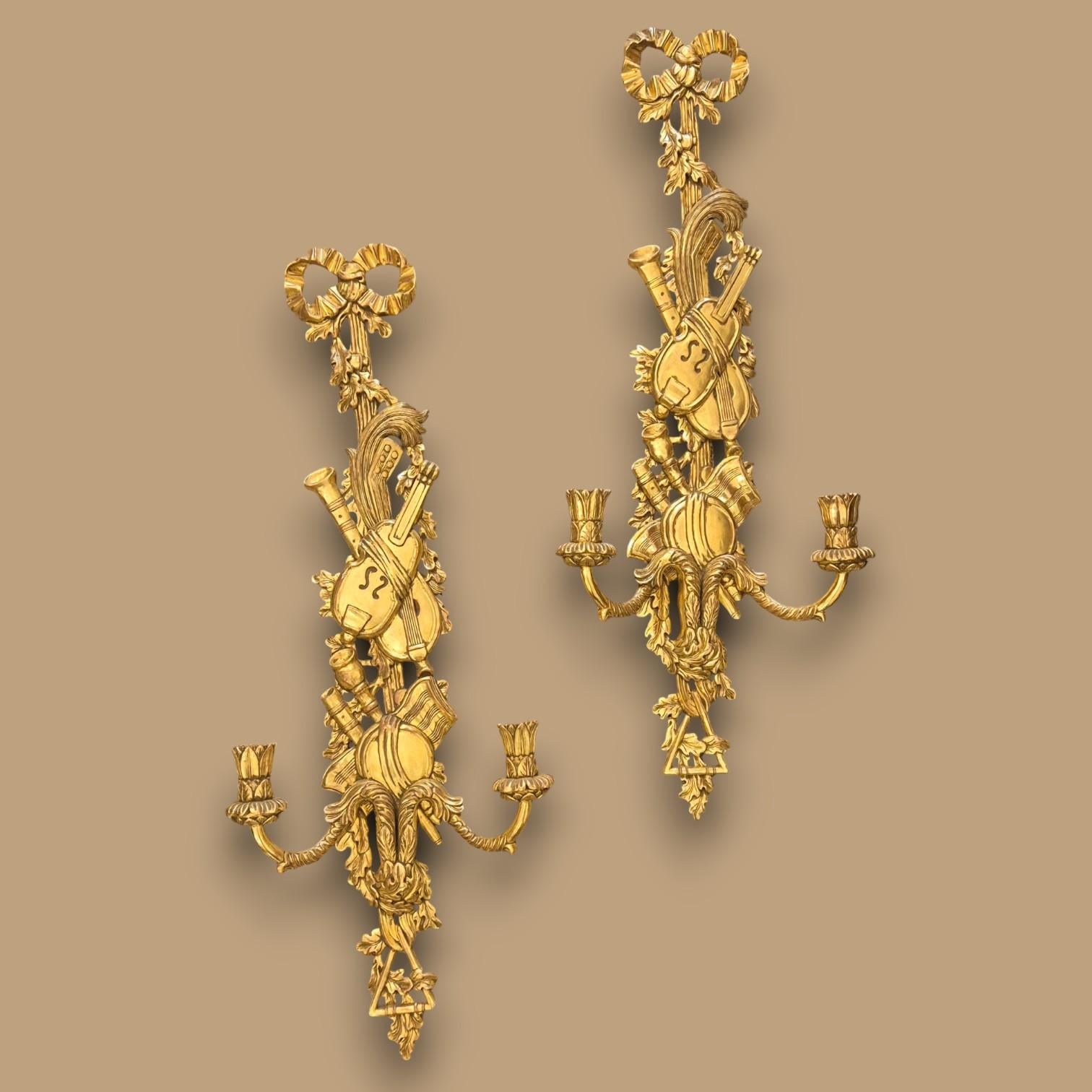 Magnifica e imponente coppia di appliques a due luci in legno dorato in stile Luigi XVI, XIX secolo.

Decorazioni intagliate a tema musicale, con numerosi strumenti: violino, chitarra, flauto, clarinetto, tamburello, campane, triangolo e uno
