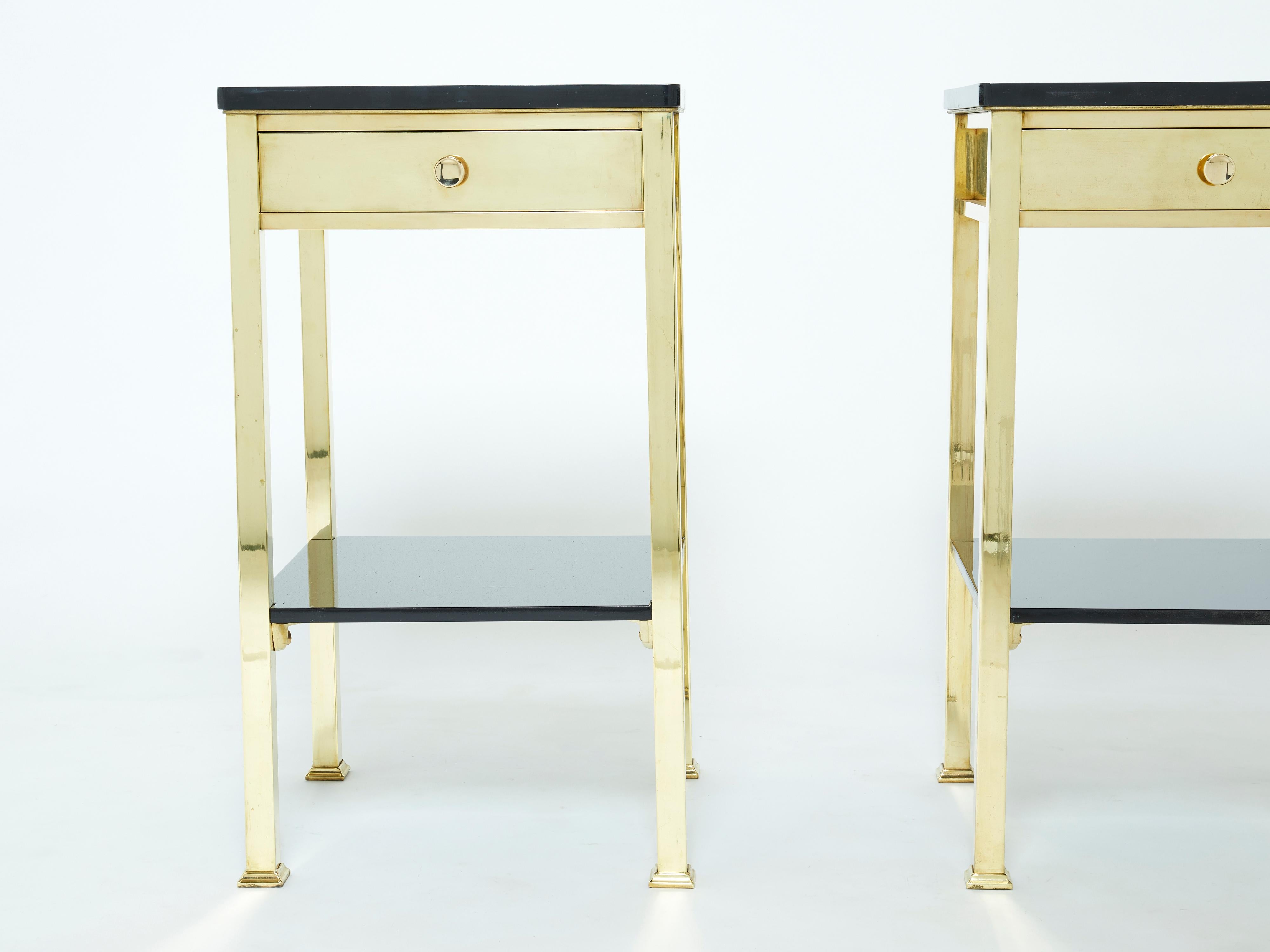 This beautiful pair of night stands or end tables were produced in France in the early 1960s. They are heavy and really quality made, with solid brass everywhere from the feet to the drawers and handles, topped with two tier black lacquered tops and