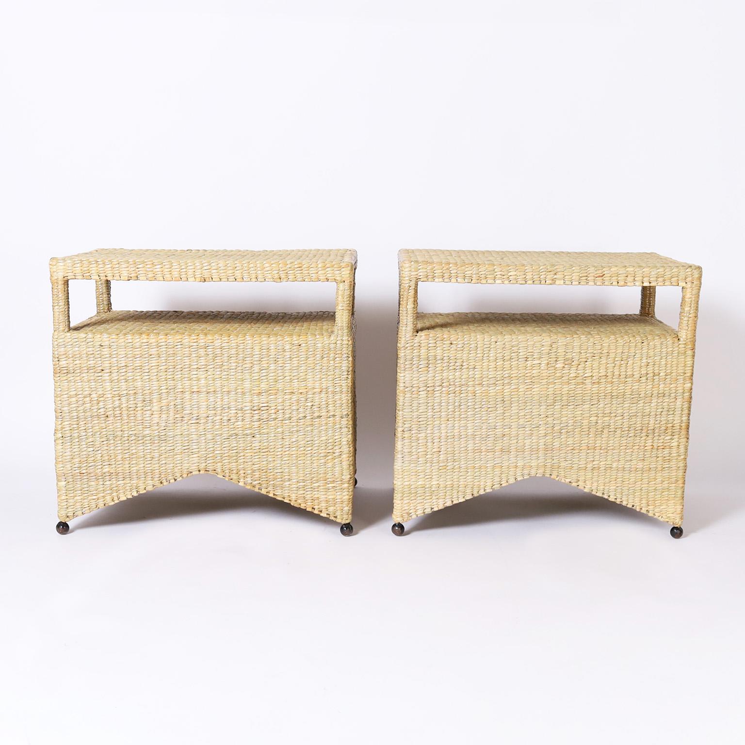 Pair of wicker stands or tables with two tiers crafted in reed expertly wrapped over a sturdy metal frame with ball feet, exclusively designed and offered by F.S. Henemader as part of the FS Flores Collection.