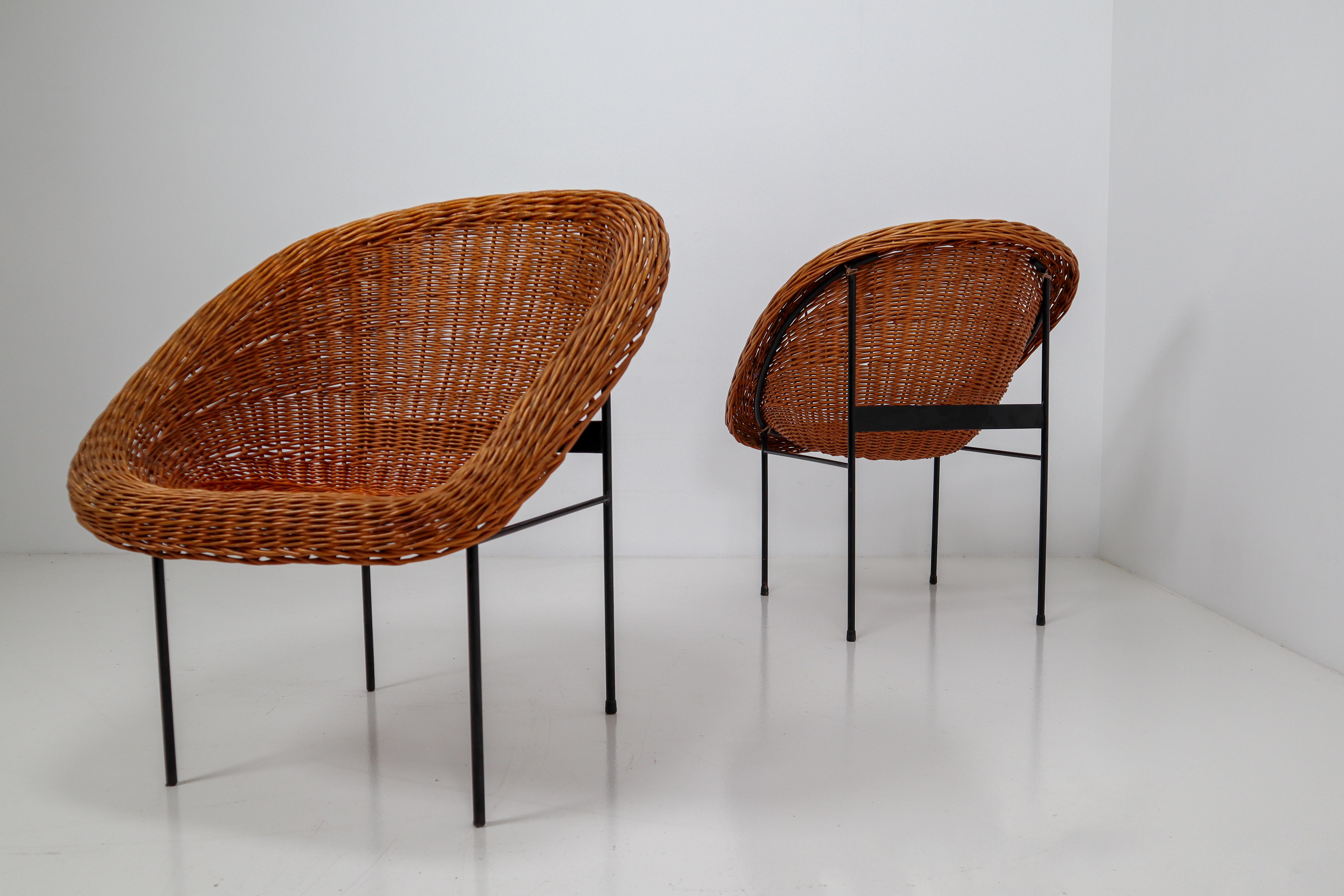 Pair of two wicker midcentury easy chairs designed and produced in France during the 1960s. The chairs are made from handwoven wicker for the seat that is formed into a basket. The frame is made of black lacquered steel. They are comfortable to sit