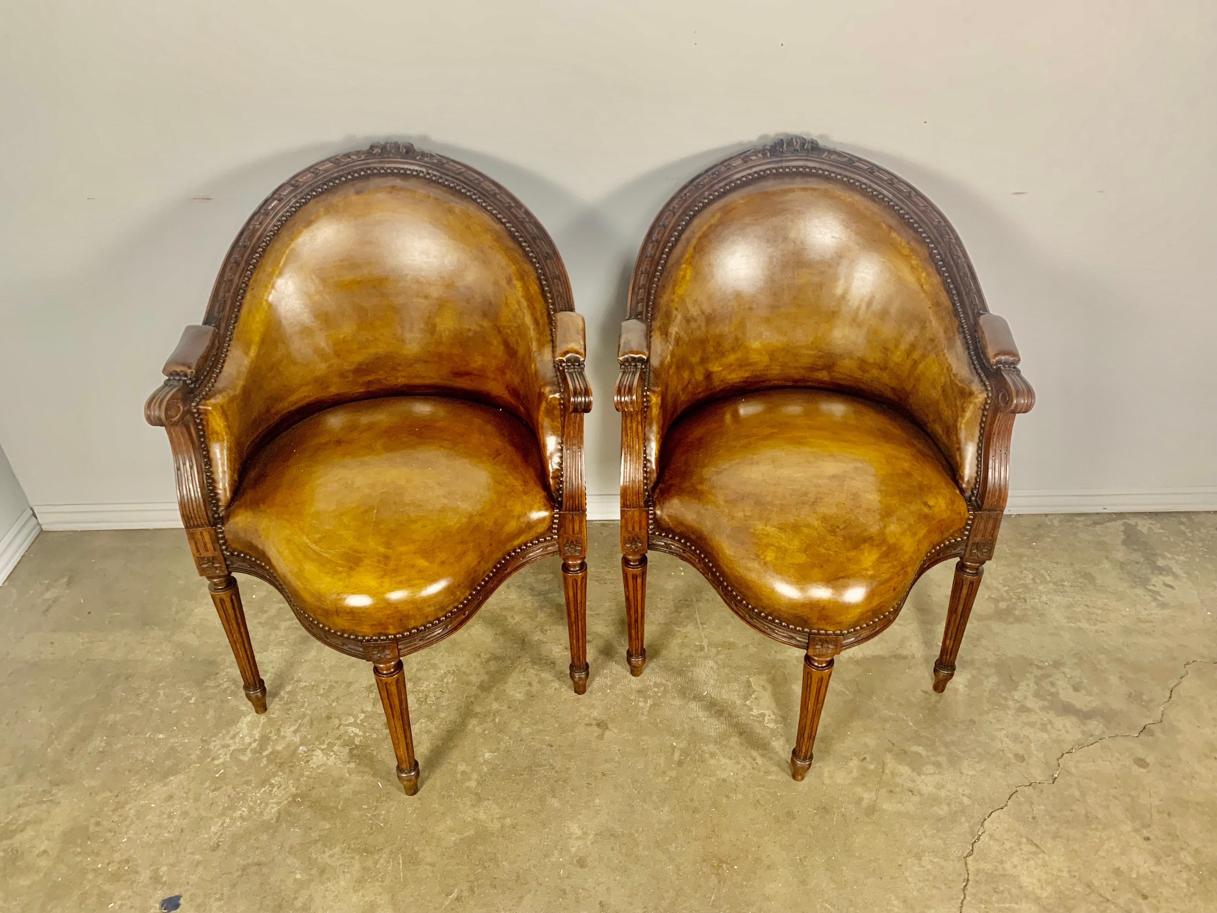 Pair of unique French Louis XVI style armchairs upholstered in a warm tobacco colored leather with nailhead trim detail. The chairs stand on four straight fluted legs. A. great pair of occasional chairs for almost any decor.