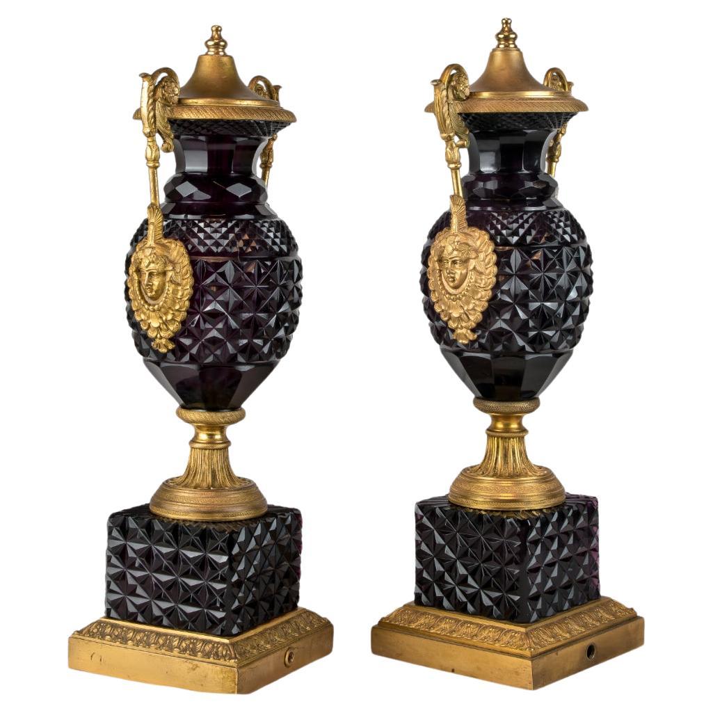 Pair of Austrian Ormolu mounted Amethyst Paste Urns with lattice design throughout. Flanked by two mounted Bacchic mascarons wearing large beaded necklaces and foliate scrolling handles. The deep plum glass is hand cut with prismatic lattice