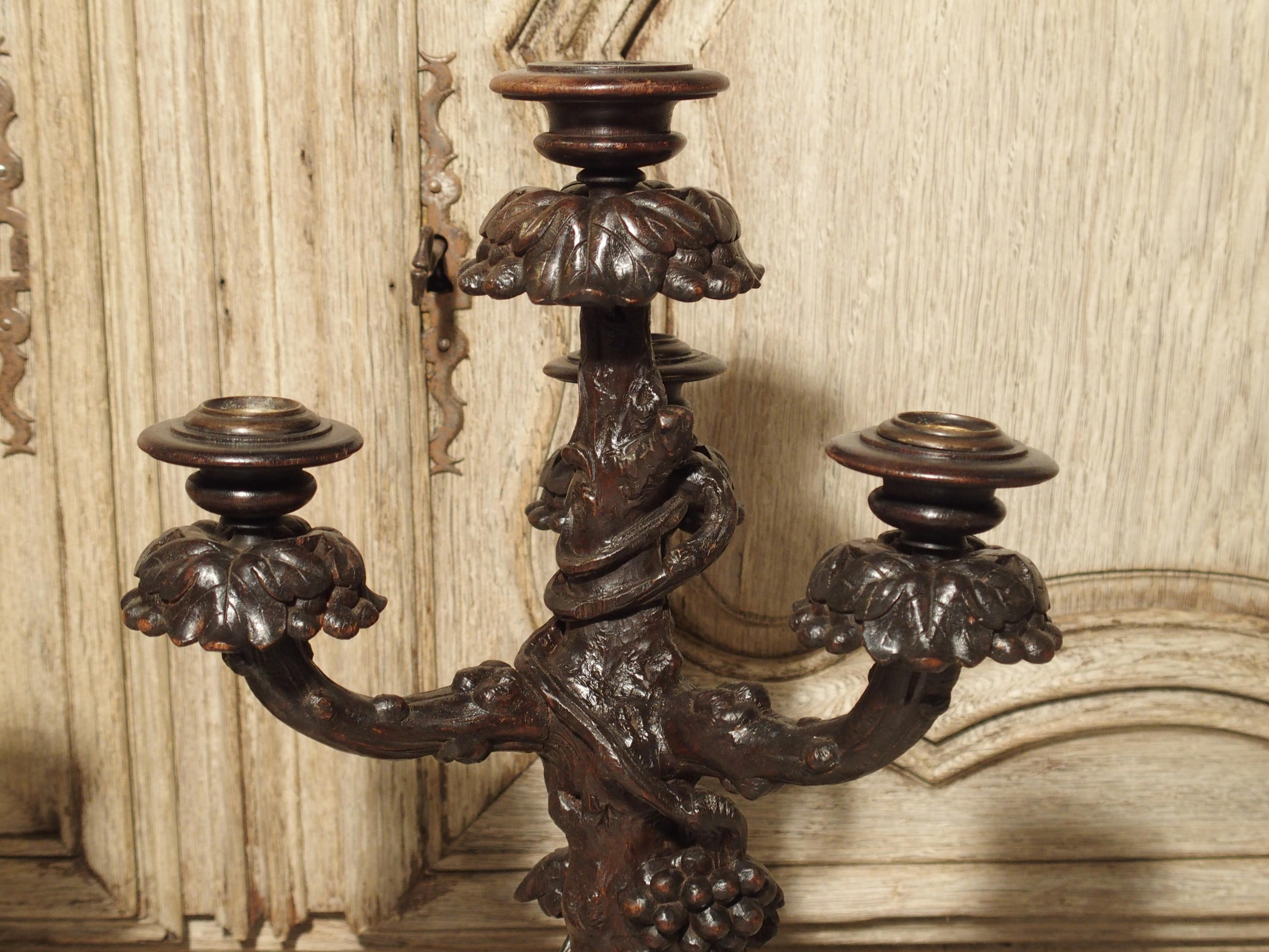This unusual pair of Black Forest, wooden candelabras have foliate motifs of branches with bunches of grapes and leaves set into a wooded ground. The grain of the wood is deep and realistically carved. There are four candle cups on each candelabra