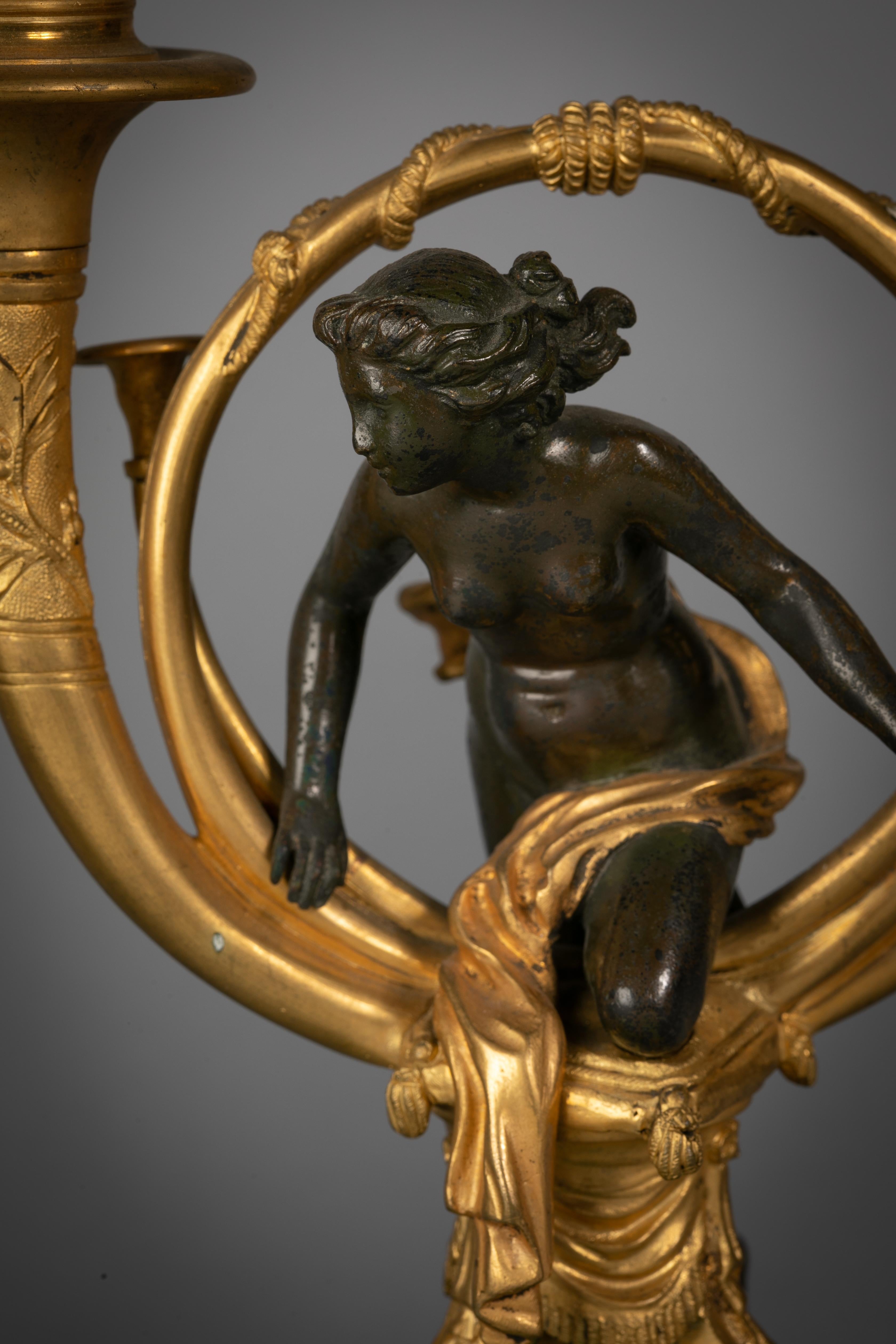 Zwei ungewöhnliche Kandelaber aus vergoldeter und patinierter Bronze und Malachit, französisch, um 1850

Die beiden weiblichen Figuren in einem doppelten Trompetenmotiv sitzen oder knien auf dreiteiligen Fußschemeln mit Quasten. Der zweiteilige