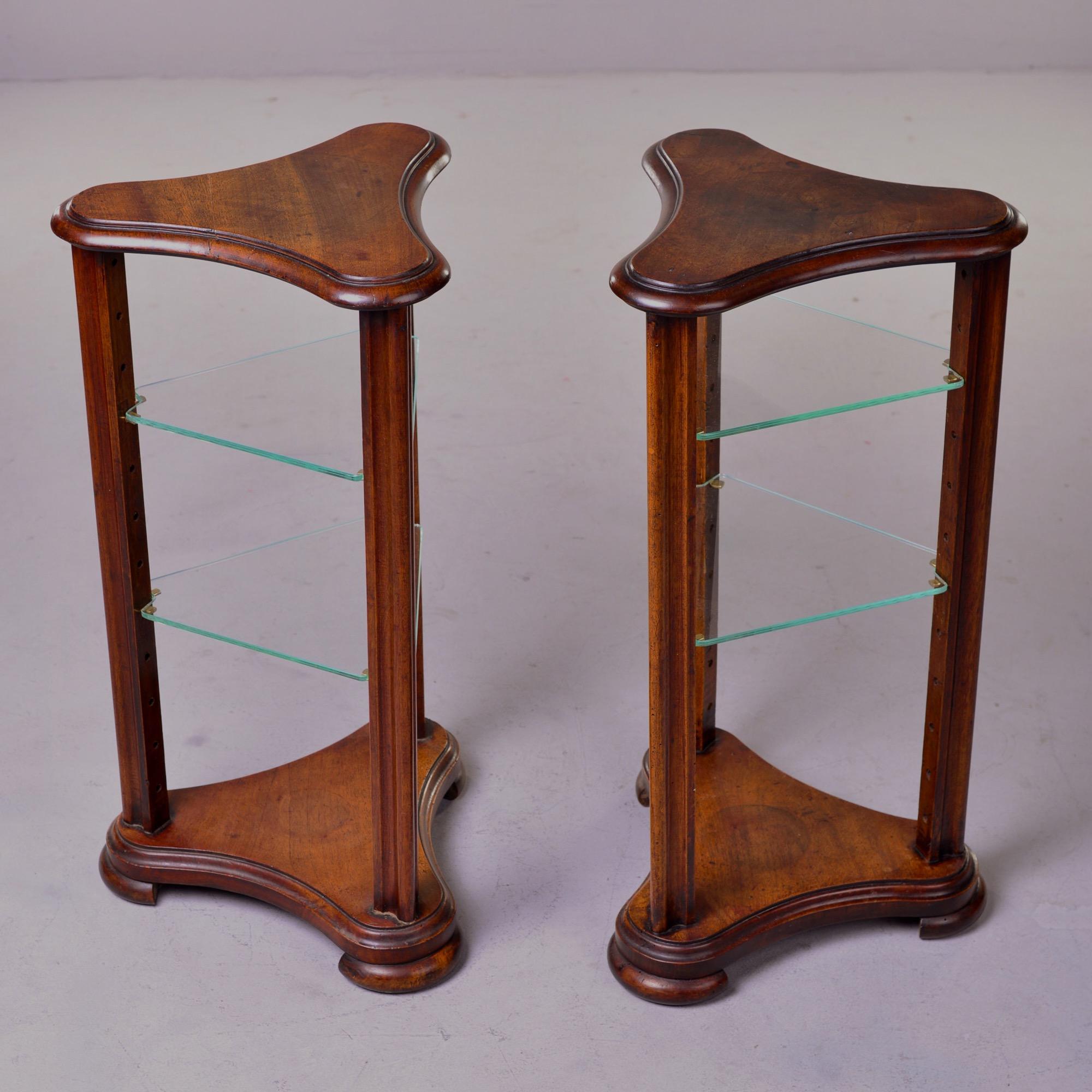 Found in England, this pair of stands or small side tables are made of walnut with a trefoil top and base and two glass shelves each. Shelf heights are adjustable. Unknown maker. Sold and priced as a pair.