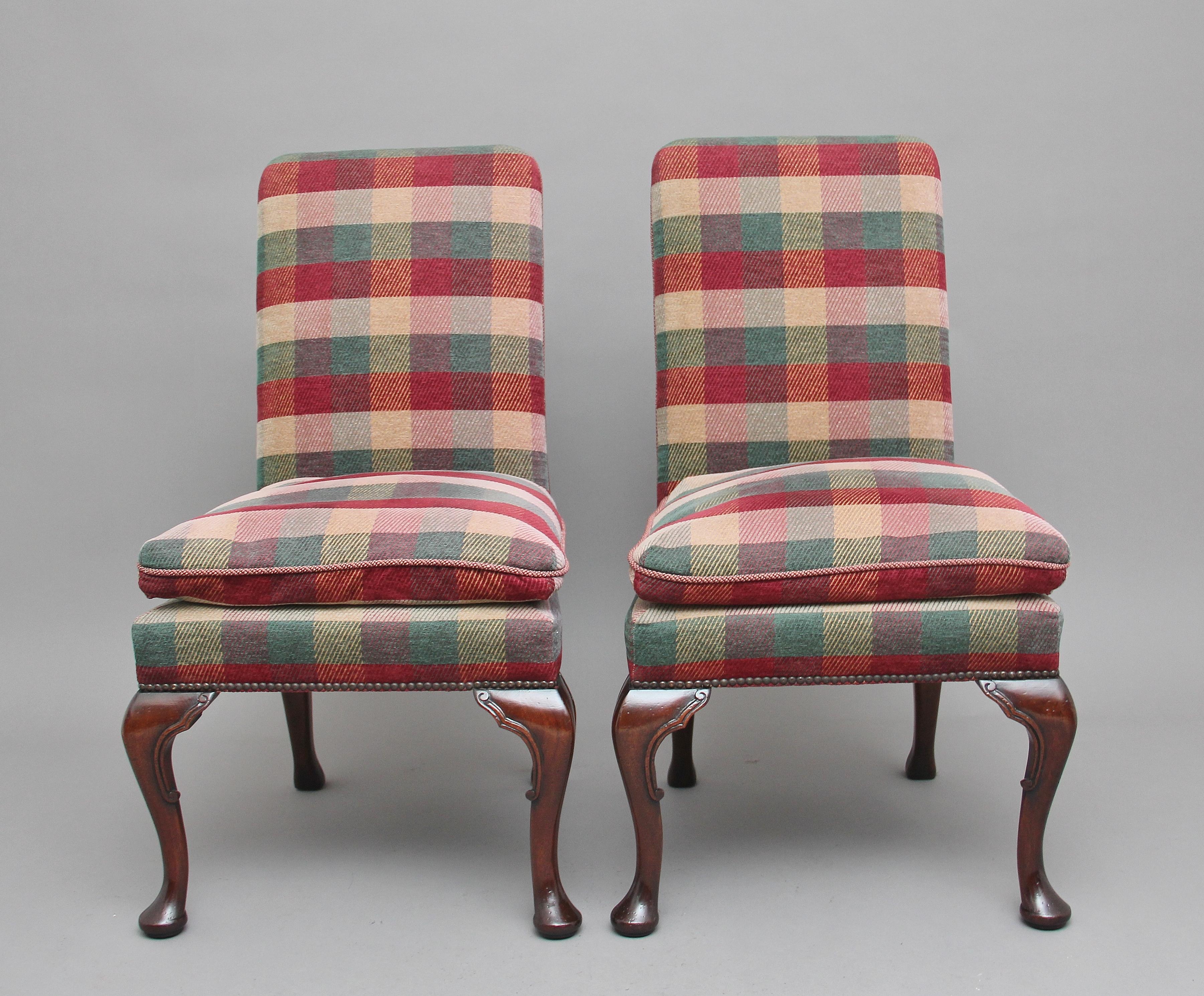 A pair of mid-20th century upholstered chairs in the George I style, the chairs upholstered in a tartan fabric with brass stud decoration, having high backs and an attached cushioned seat, supported on front carved cabriole legs ending with a