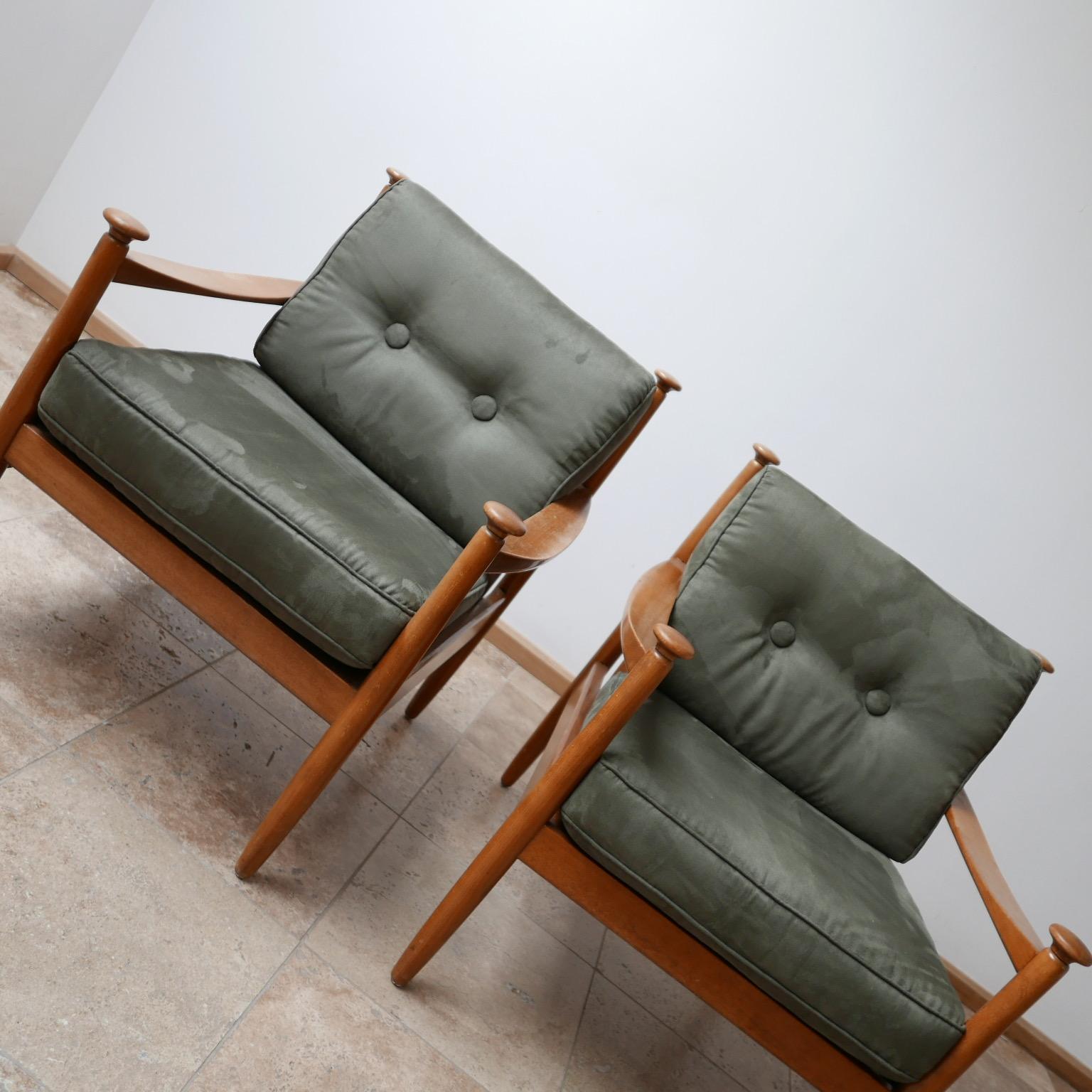 A pair of midcentury armchairs. 

Unattributed but clearly well formed design. 

The arm rests terminate in a turned ovals that are strangely tactile and comforting. 

The upholstery is clearly new (not by us) but is over stuffed in some